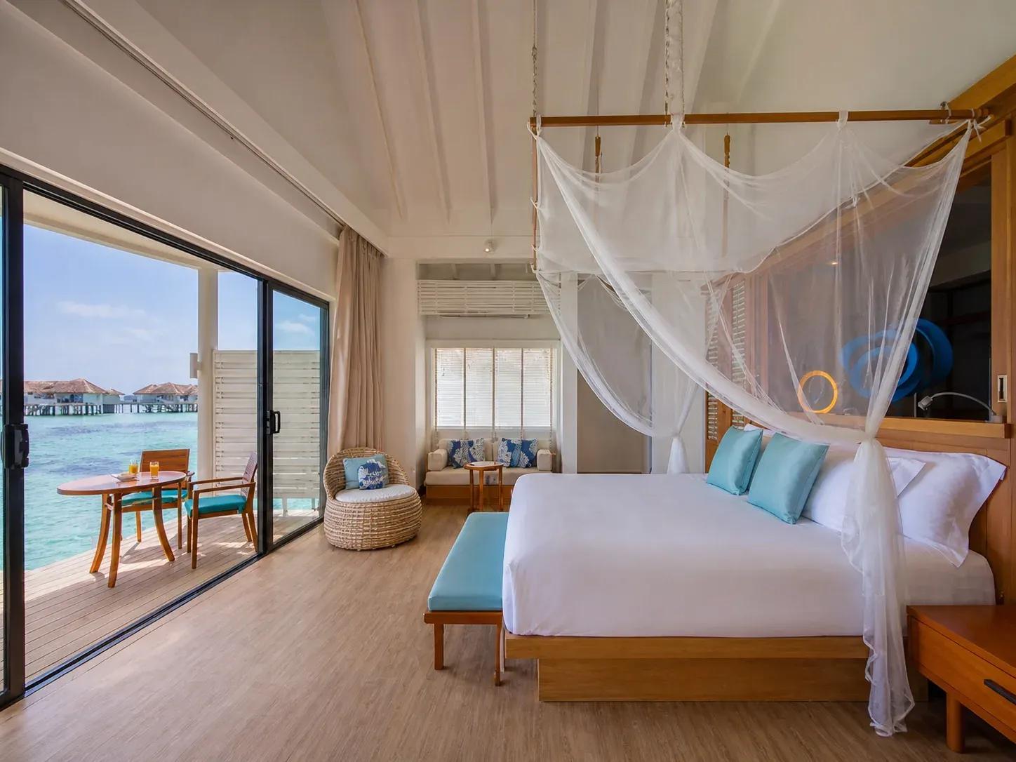 Camera da letto della Club Sunset Overwater Villa with Pool con letto a baldacchino e terrazza vista mare al Centara Machchafushi Island Resort & Spa Maldives.