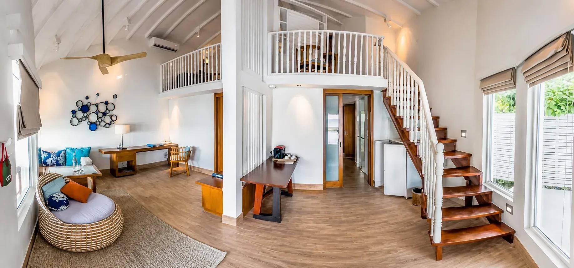 Interno della Club Two Bedroom Beach Pool Villa con scale in legno e salotto al Centara Machchafushi Island Resort & Spa Maldives.