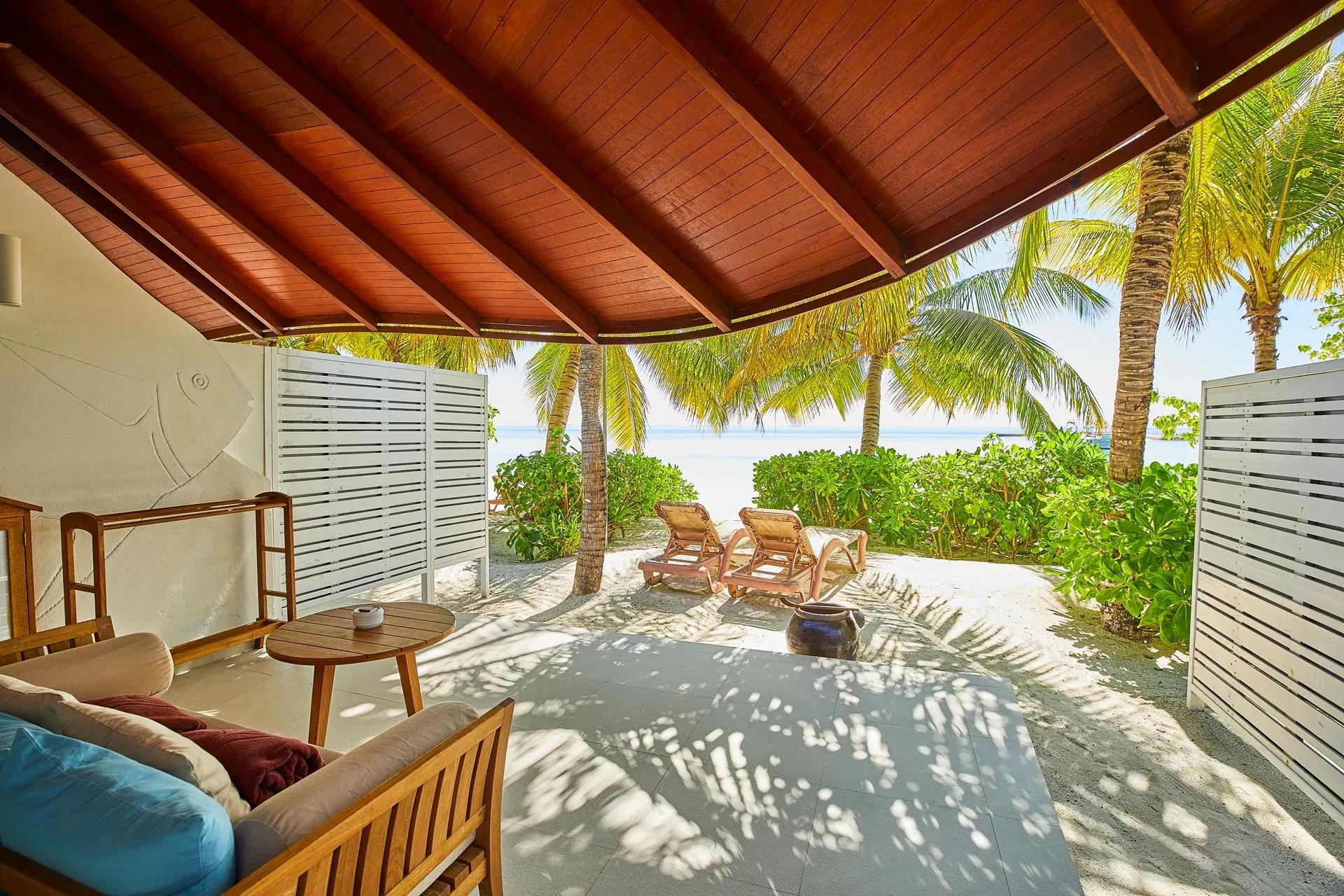 Terrazza della Duplex Beach Villa con sedute in legno e lettini sulla spiaggia del Centara Machchafushi Island Resort & Spa Maldives