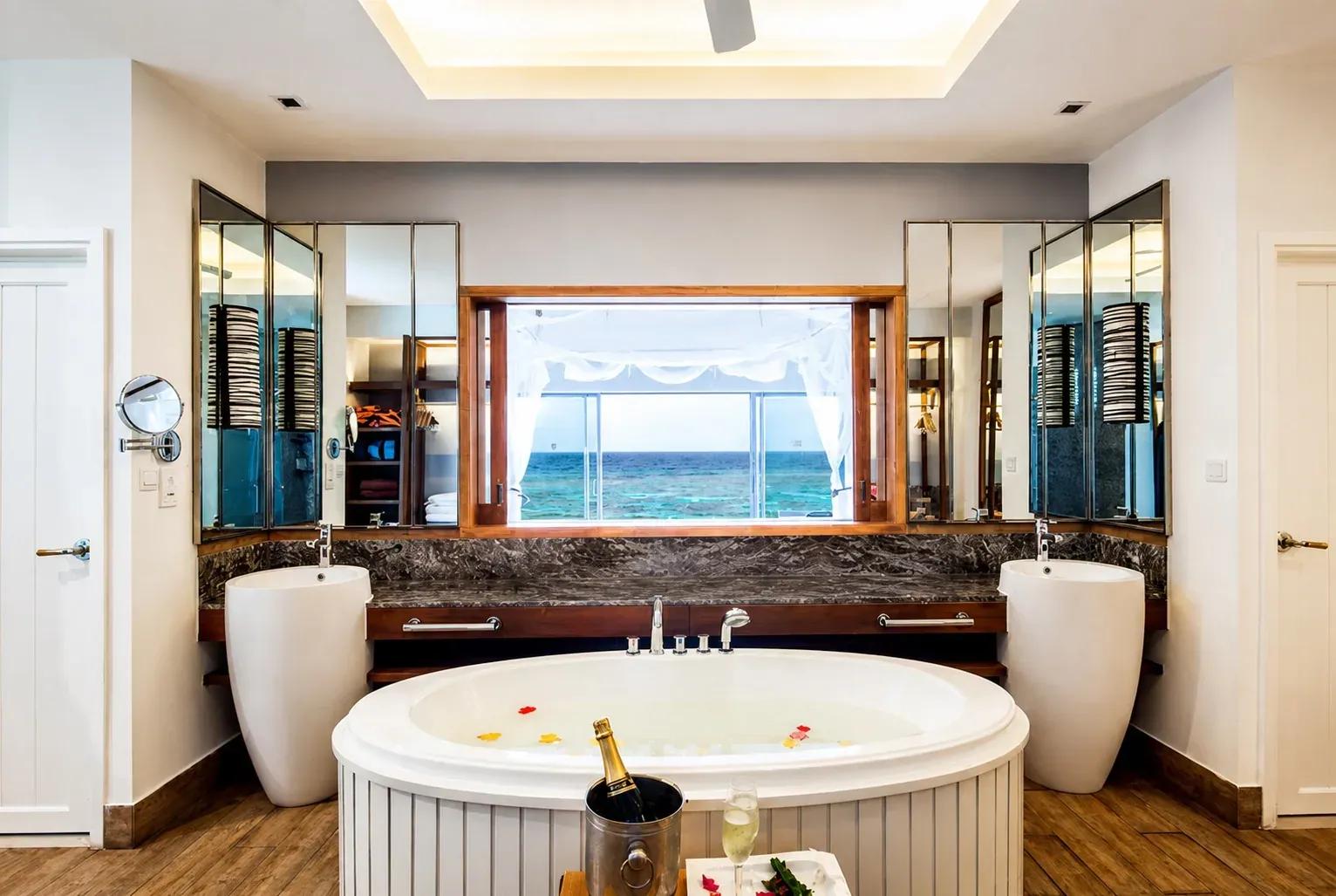 Bagno della Reethi Muraka Overwater Villa con vasca idromassaggio, lavabi e vista sull'oceano al Centara Machchafushi Island Resort & Spa Maldives.
