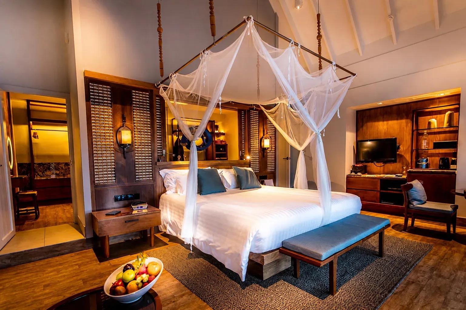 Interno della Reethi Muraka Overwater Villa con letto a baldacchino e area soggiorno al Centara Machchafushi Island Resort & Spa Maldives.