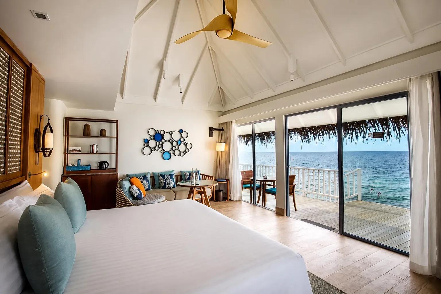 Camera da letto della Sunrise Overwater Villa con vista sull'oceano e terrazza al Centara Machchafushi Island Resort & Spa Maldives.