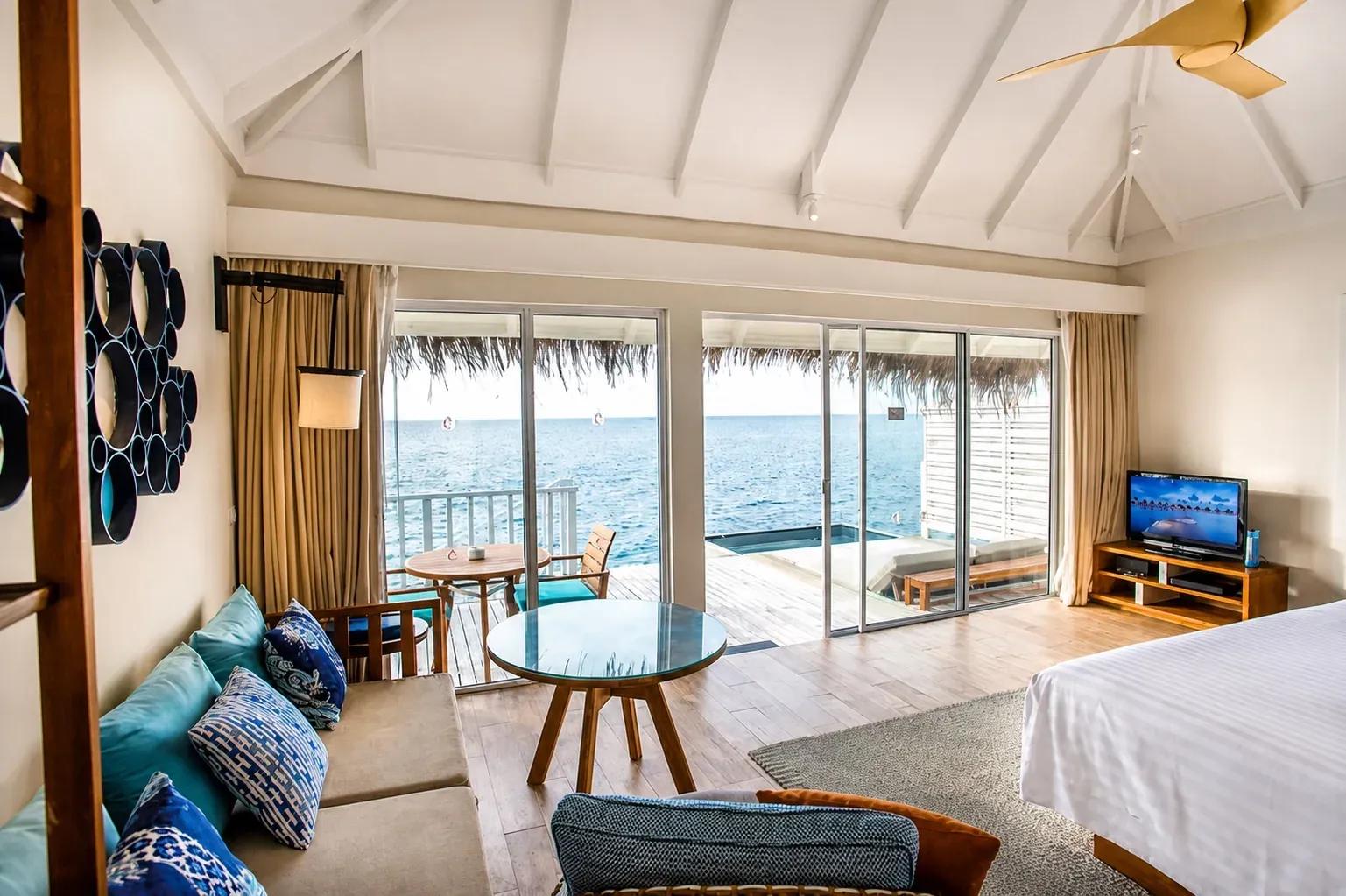 Interno della Sunrise Overwater Villa con salotto e vista sull'oceano al Centara Machchafushi Island Resort & Spa Maldives.