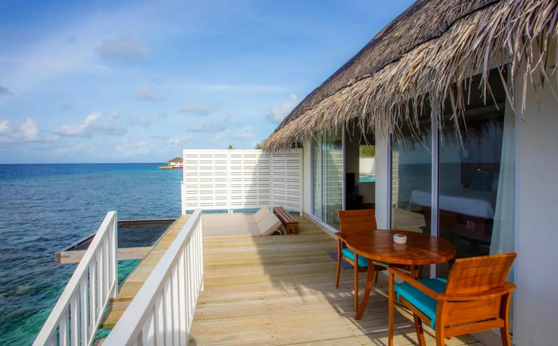 Terrazza della Sunset Overwater Villa con tavolo in legno e vista sull'oceano al Centara Machchafushi Island Resort & Spa Maldives.
