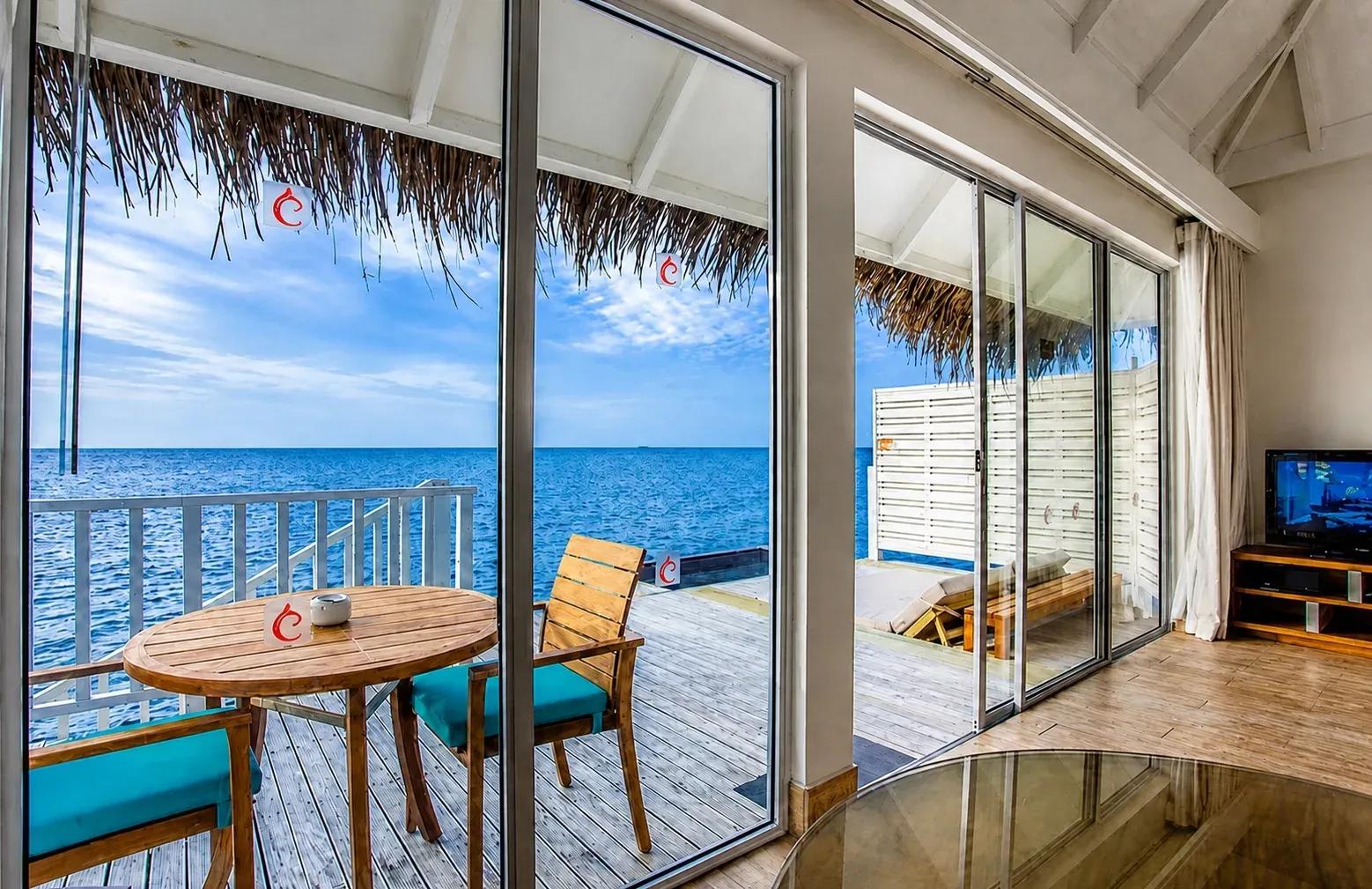 Vista dall'interno della Sunset Overwater Villa con terrazza e sedie in legno al Centara Machchafushi Island Resort & Spa Maldives.
