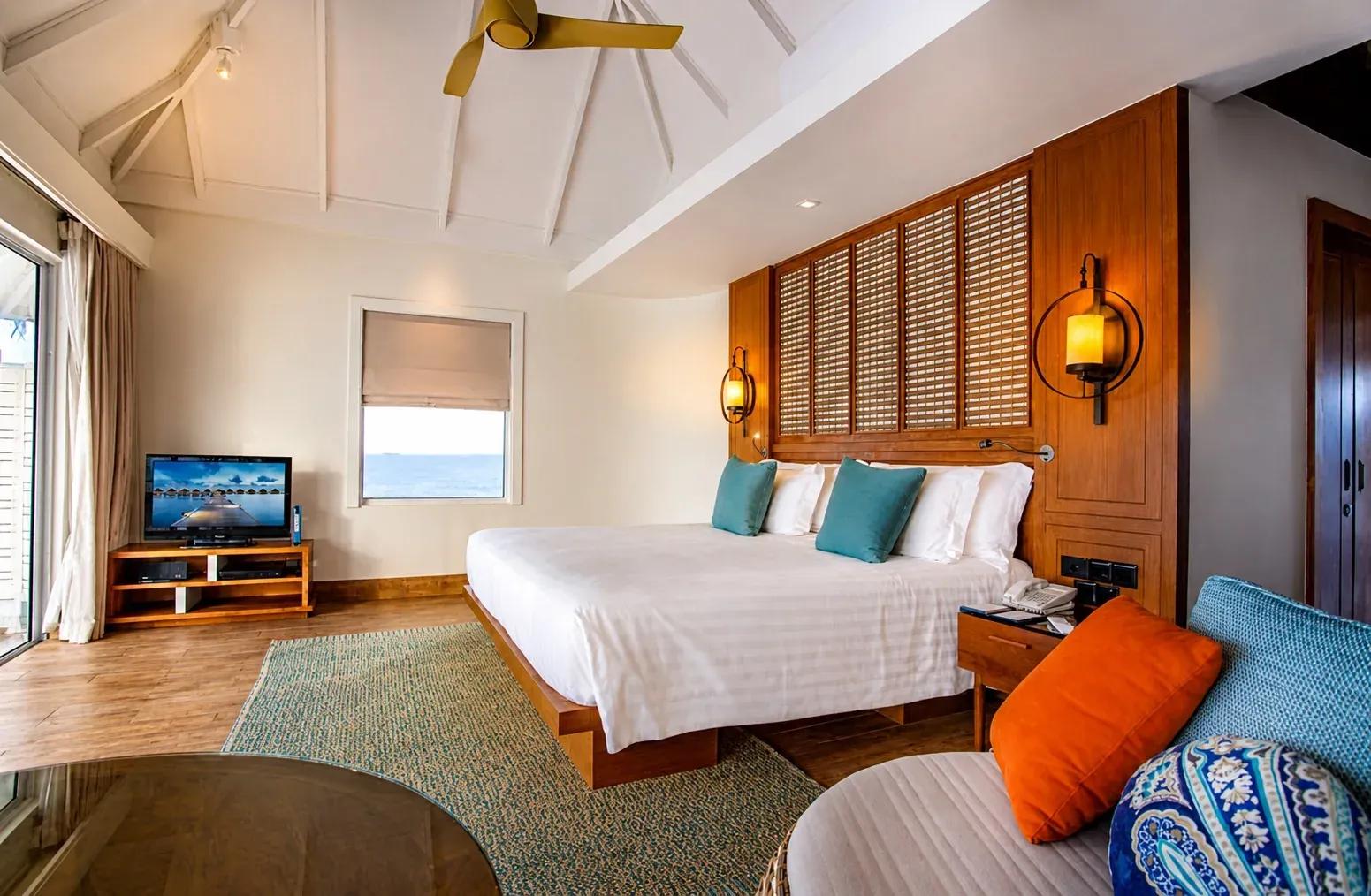 Interno della Sunset Overwater Villa con letto king-size e vista sull'oceano al Centara Machchafushi Island Resort & Spa Maldives.