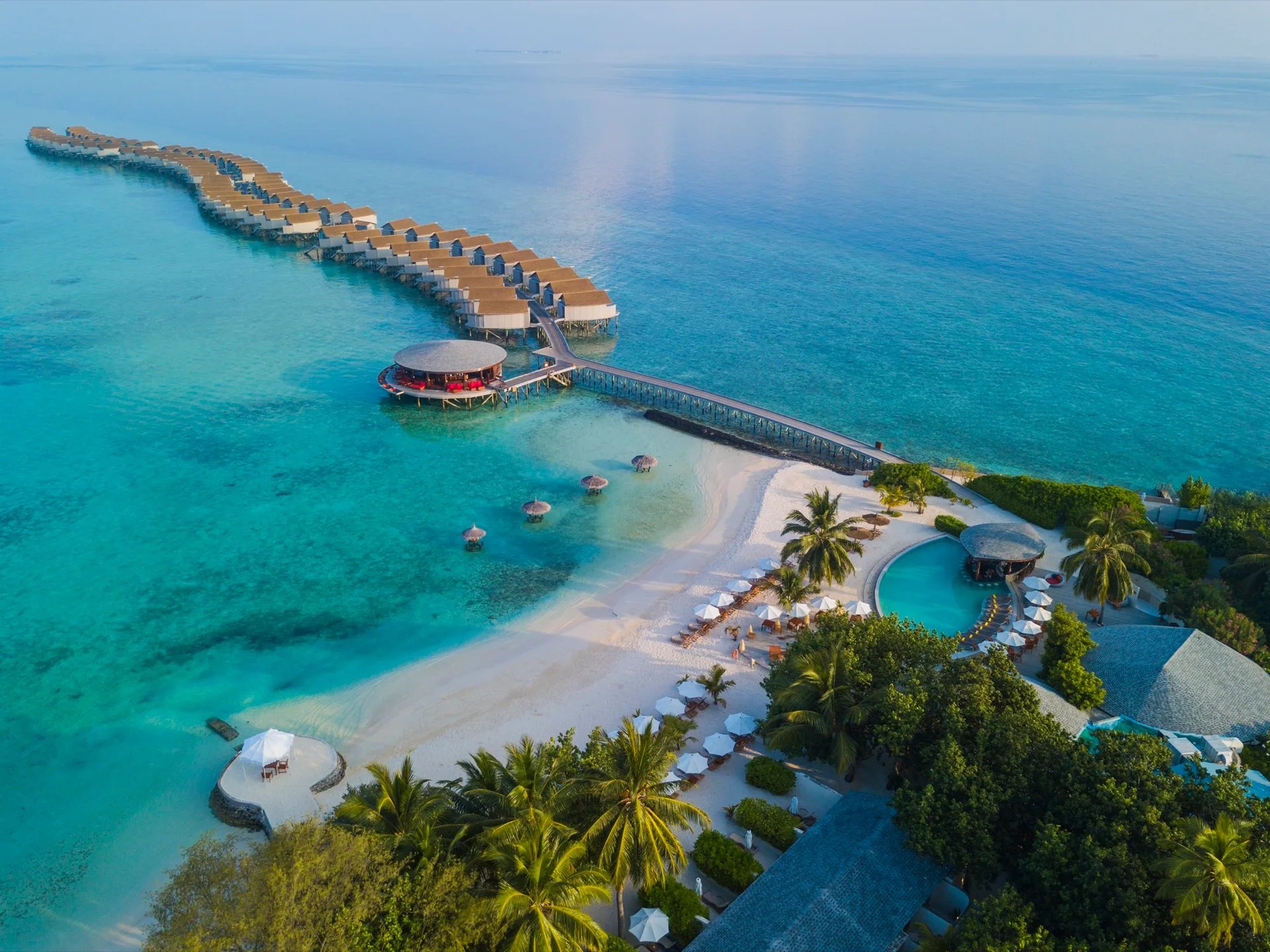 Veduta aerea del Centara Ras Fushi Resort & Spa Maldives con ville sull'acqua e spiaggia bianca.