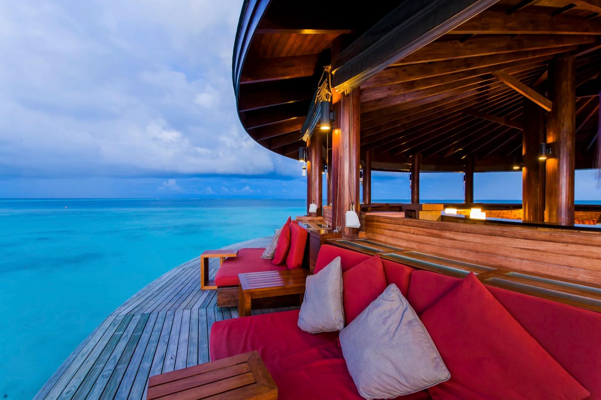 Area salotto con cuscini rossi sul mare al Centara Ras Fushi Resort & Spa Maldives