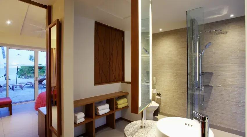 Interno della Lagoon View Beach Villa with Swirl Pool con bagno moderno e vista su terrazza con lettini al Centara Ras Fushi Resort & Spa Maldives.