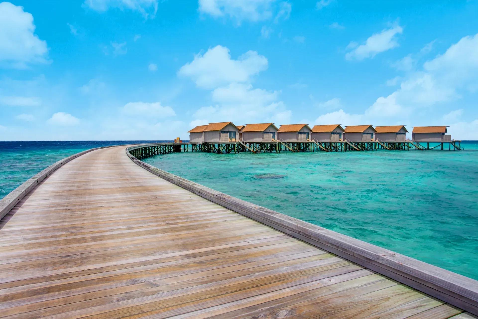 Passerella in legno verso Overwater Villa sul mare cristallino del Centara Ras Fushi Resort & Spa Maldives.