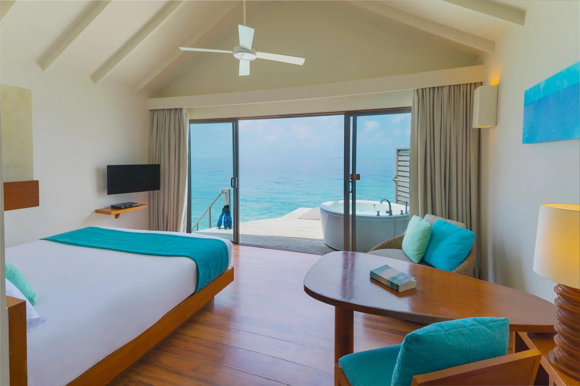 Interno della Sunset Overwater Villa con letto e vasca vista mare al Centara Ras Fushi Resort & Spa Maldives