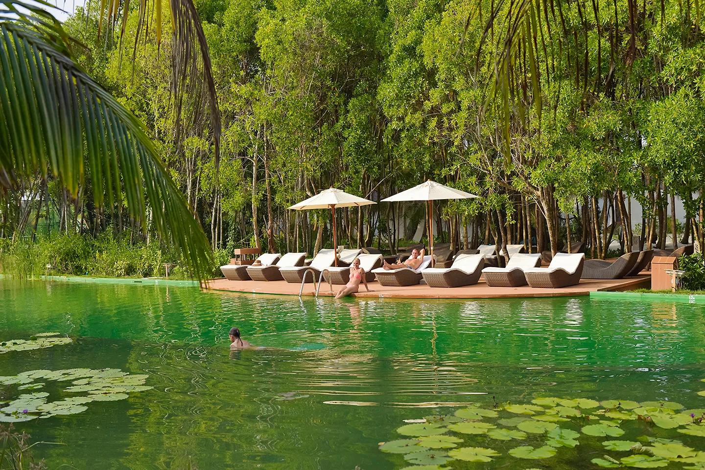 Ospiti si rilassano nel lago d'acqua dolce del Dreamland The Unique Sea And Lake Resort Spa, nuotando tra le ninfee o prendendo il sole sui lettini del solarium in legno, immerso in una fitta vegetazione.