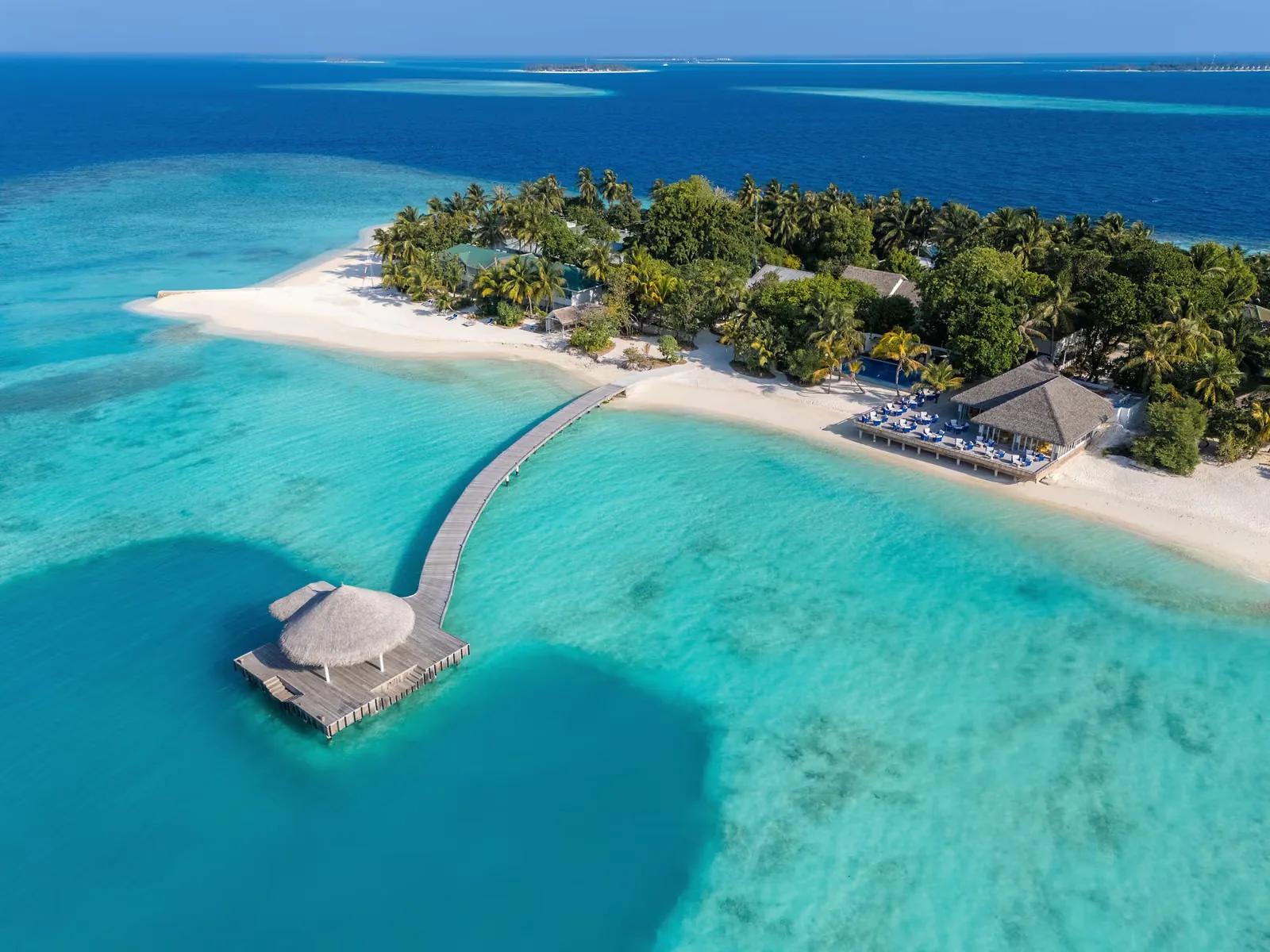 Vista aerea di Eri Maldives con pontile sull'acqua turchese, spiaggia di sabbia bianca, fitta vegetazione e strutture sulla riva.