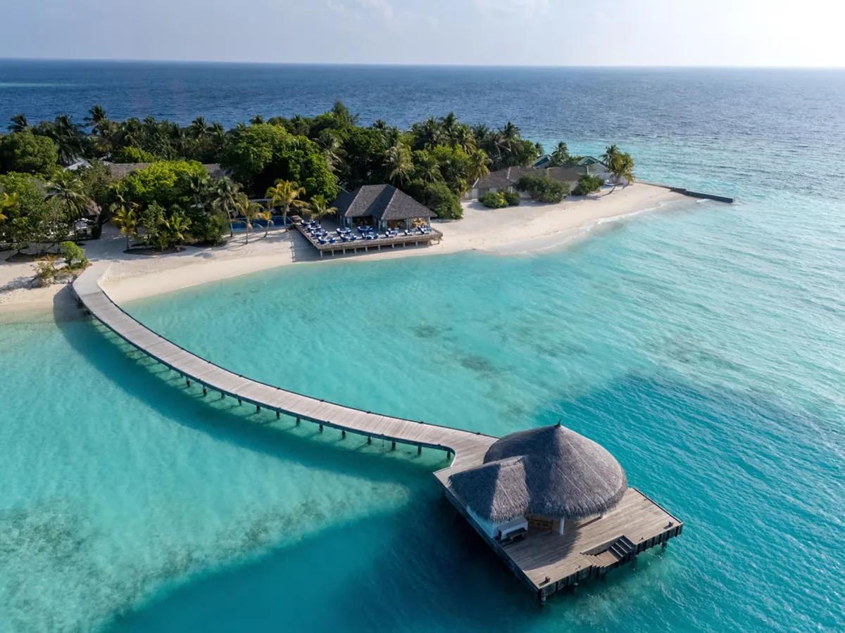 Vista aerea di Eri Maldives con pontile curvo in legno sulla laguna turchese, padiglione sull'acqua, spiaggia bianca e terrazza fronte mare