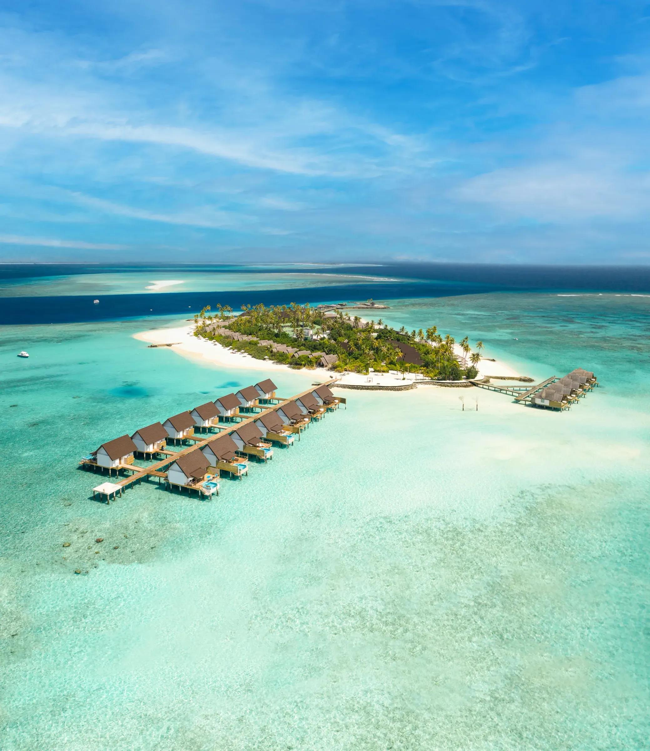 Vista aerea dell'isola tropicale e delle ville sull'acqua del Fushifaru Maldives circondate da acque turchesi.