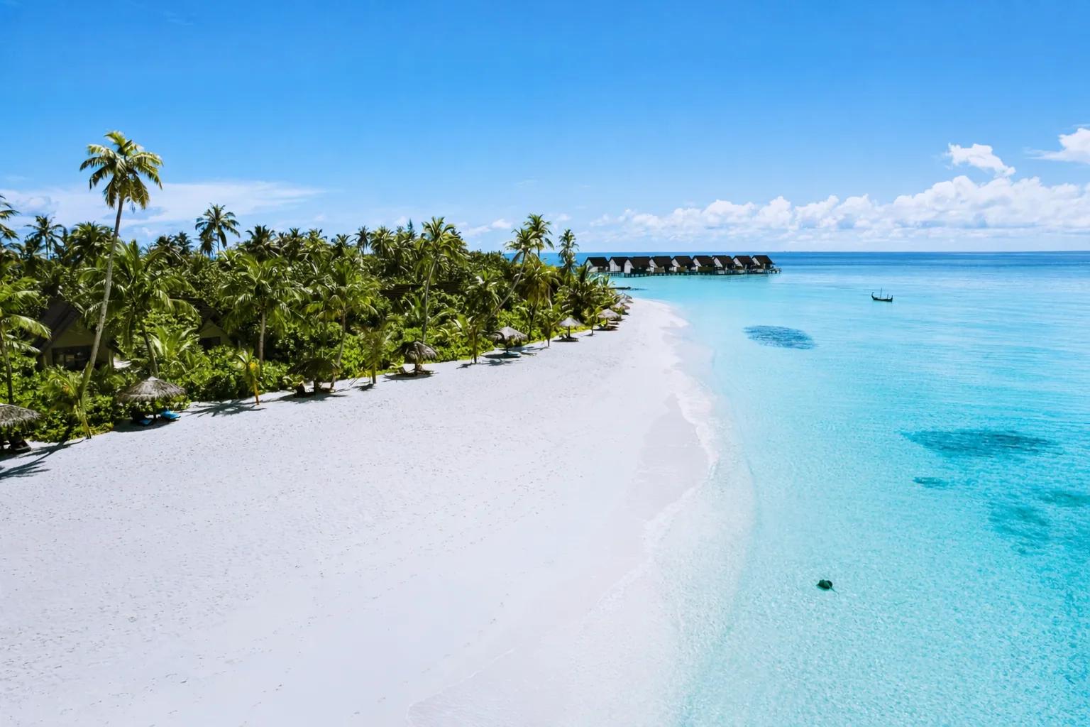 Spiaggia di sabbia bianca con palme e ville sull'acqua al Fushifaru Maldives.