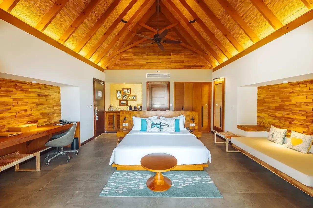Interno della Beach Duplex Villa con letto matrimoniale e area salotto al Fushifaru Maldives.