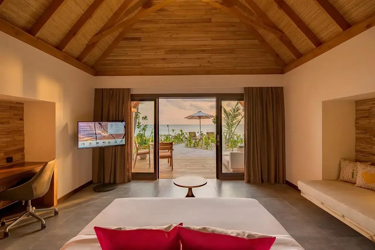 Interno della Beach Villa Sunrise con vista sul mare, terrazza e lettini al Fushifaru Maldives.