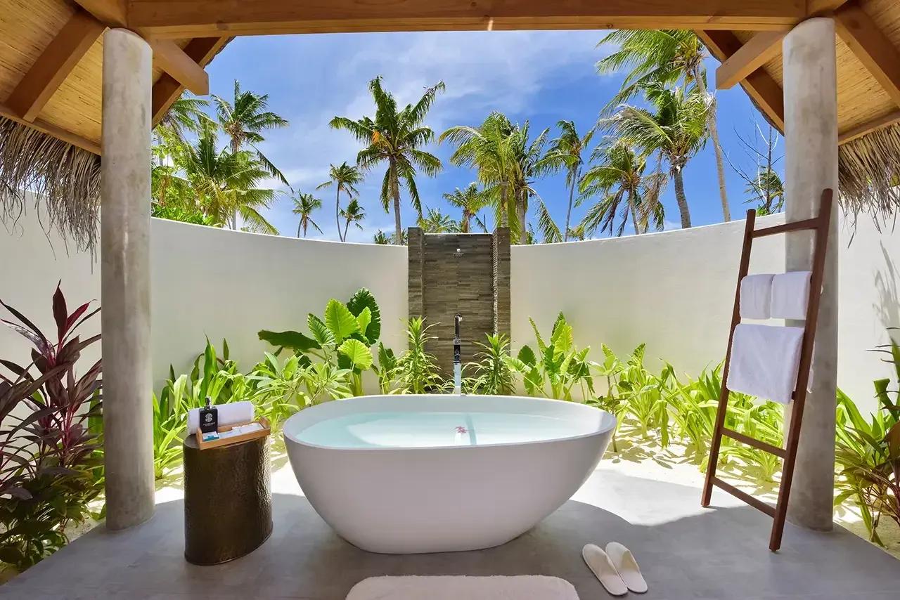 Vasca esterna circondata da vegetazione e doccia nella Beach Villa Sunset del Fushifaru Maldives.