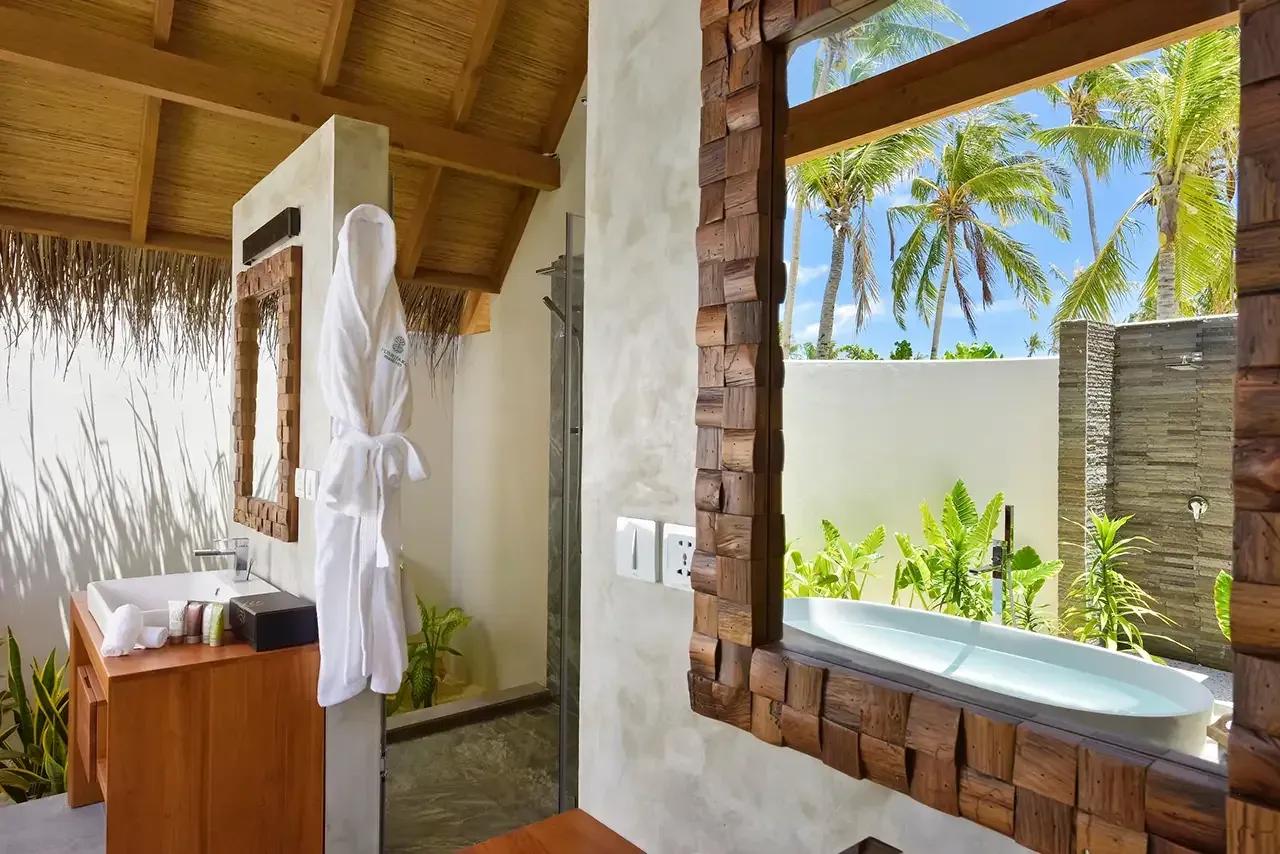 Bagno della Beach Villa Sunset con lavabo in legno, doccia esterna e vista su palme al Fushifaru Maldives.