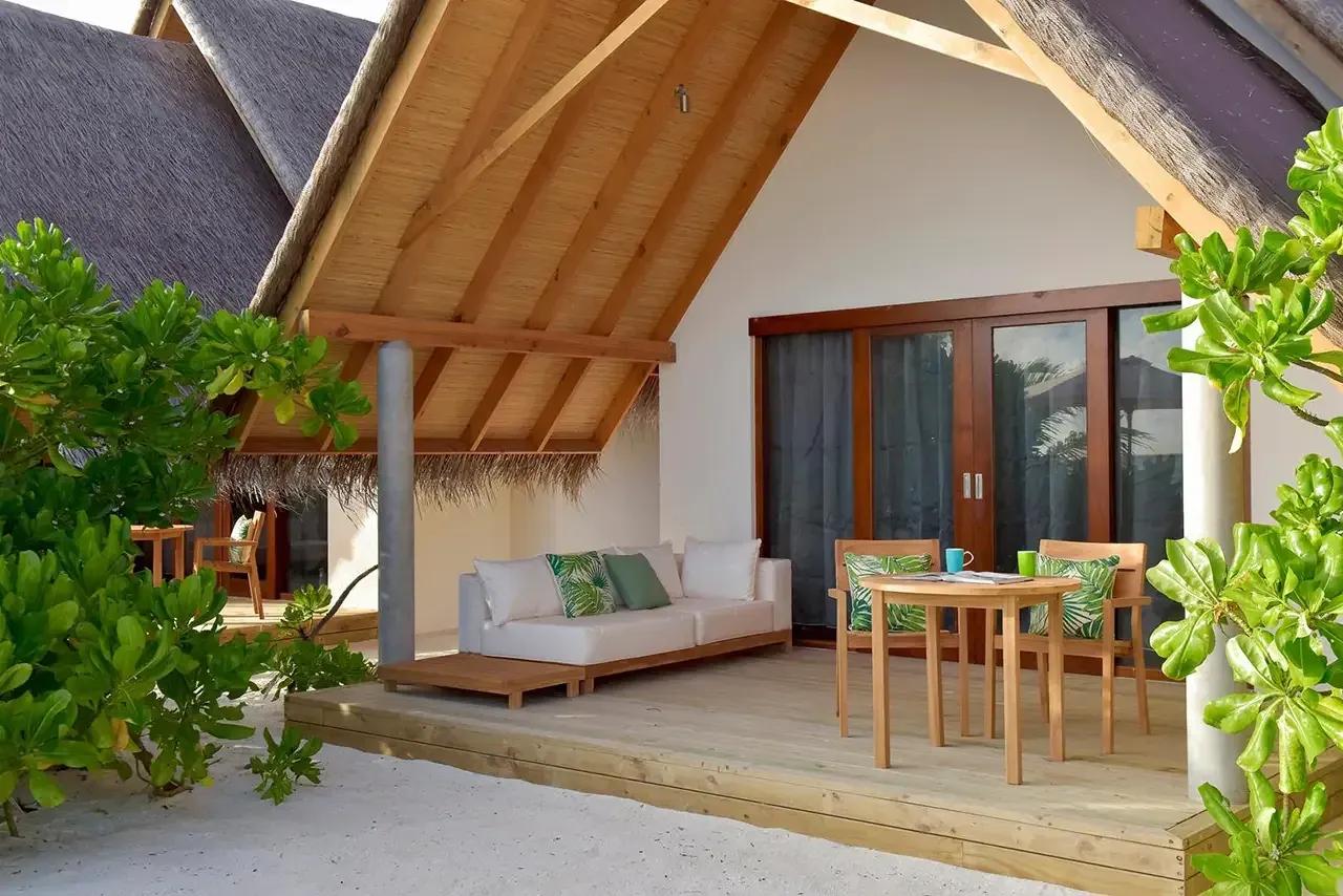 Terrazza della Beach Villa Sunset con sedute e tavolo in legno al Fushifaru Maldives.