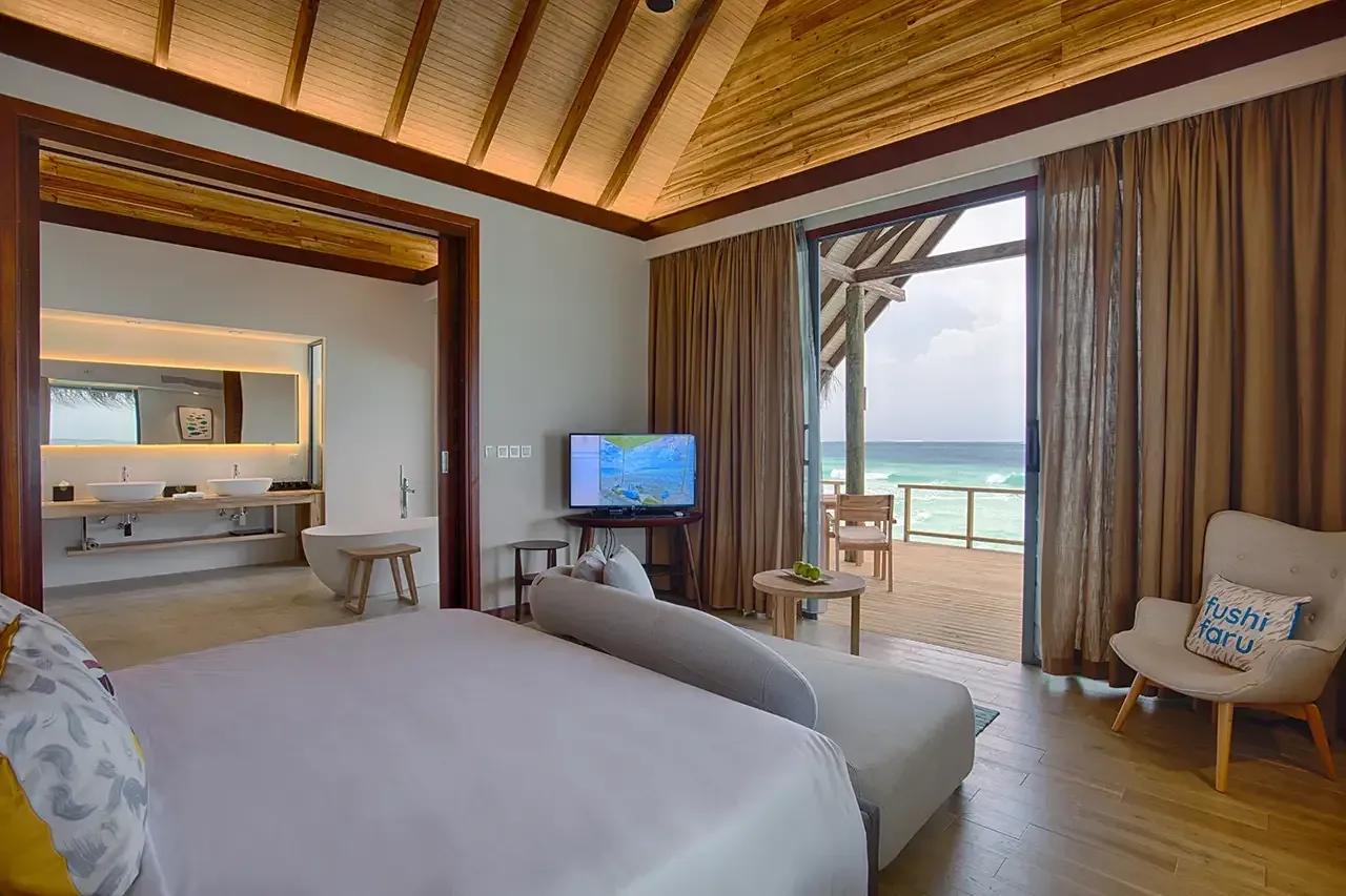 Interno della Jacuzzi Water Villa con letto, TV e terrazza vista mare al Fushifaru Maldives.