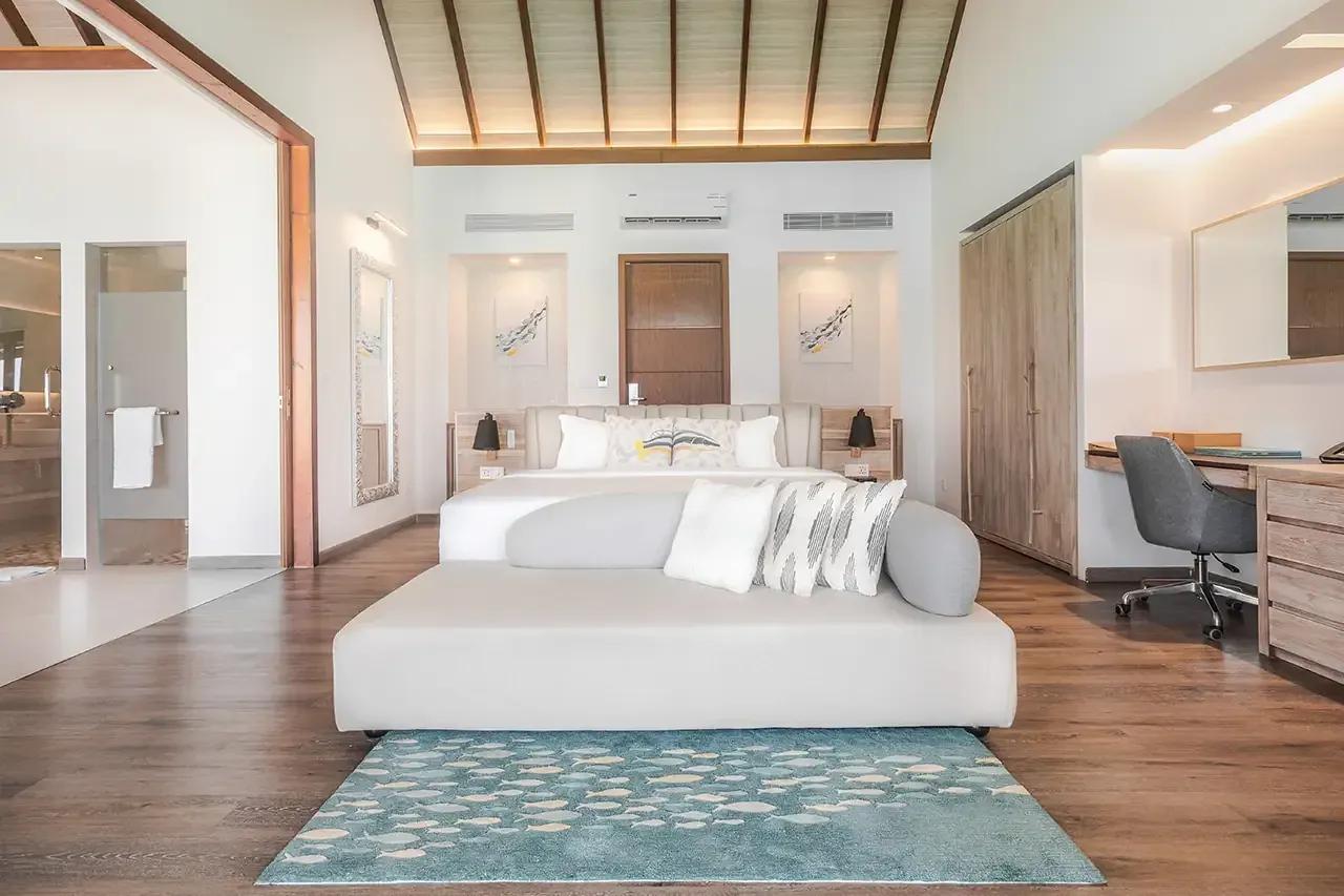 Interno della Jacuzzi Water Villa con letto, scrivania e divano al Fushifaru Maldives.