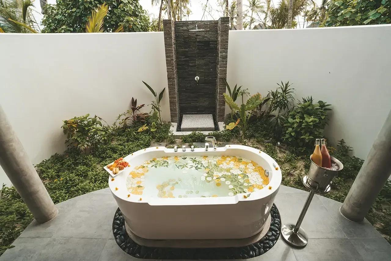 Vasca da bagno con fiori e parete doccia esterna nella Pool Beach Villa Sunrise del Fushifaru Maldives.