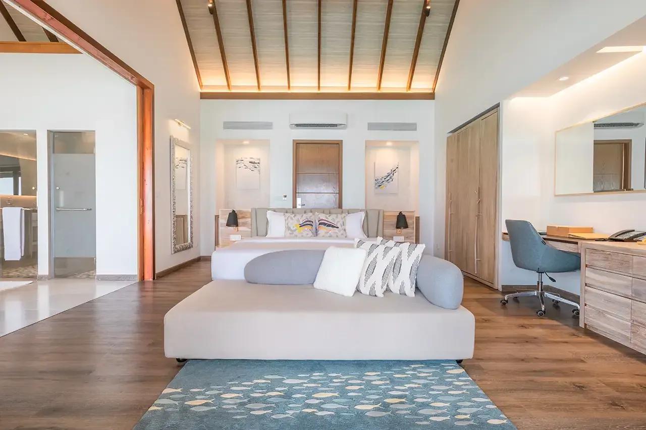 Interno della Pool Water Villa con divano grigio e zona lavoro del Fushifaru Maldives.