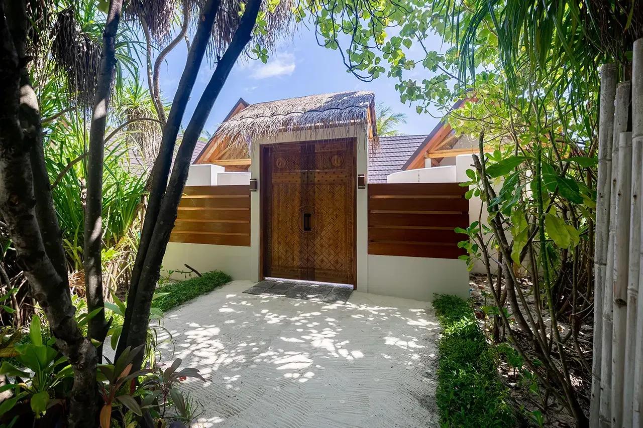 Ingresso della Premium Beach Duplex Villa con porta in legno e tetto in paglia al Fushifaru Maldives.