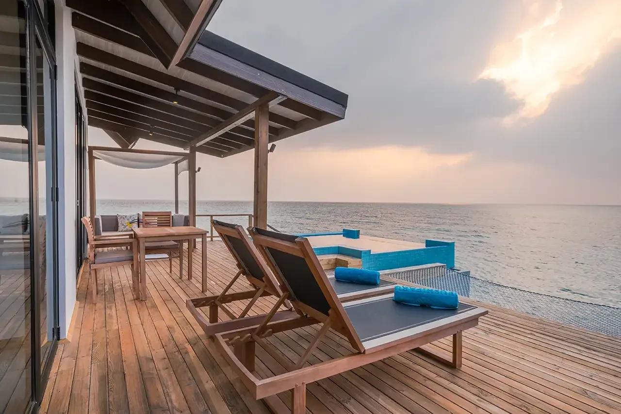 Terrazza in legno con piscina privata e lettini della premium pool water villa al Fushifaru Maldives con vista sull'oceano