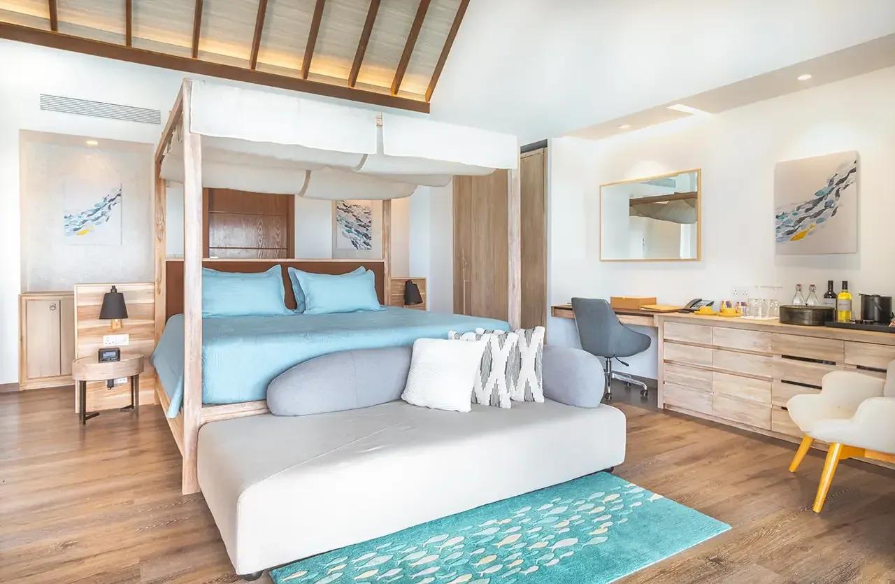 Interno della Premium Pool Water Villa con letto a baldacchino e scrivania al Fushifaru Maldives.