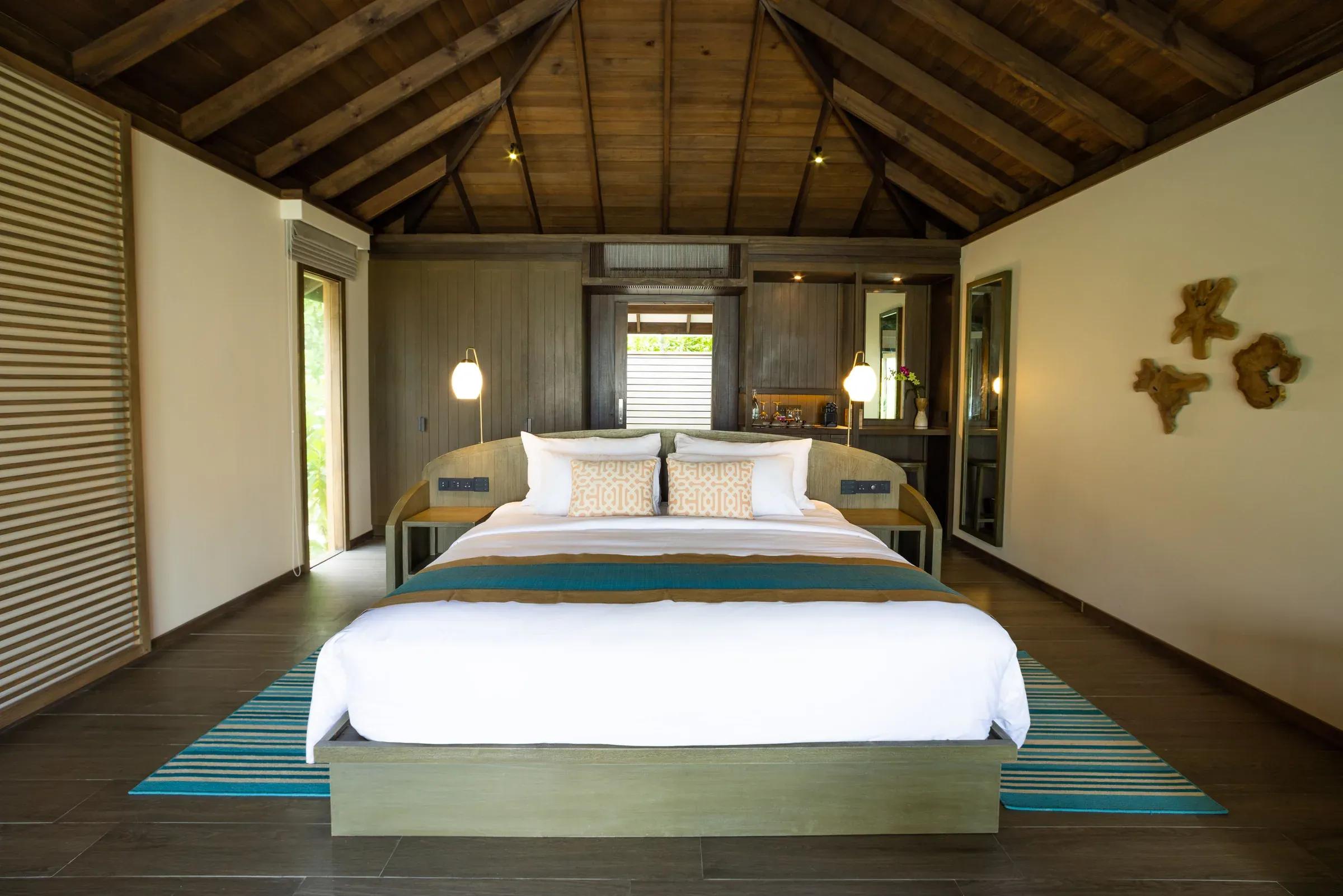 Interno della Dheru Beach Pool Villa con letto matrimoniale e soffitto in legno al Jawakara Islands Maldives.