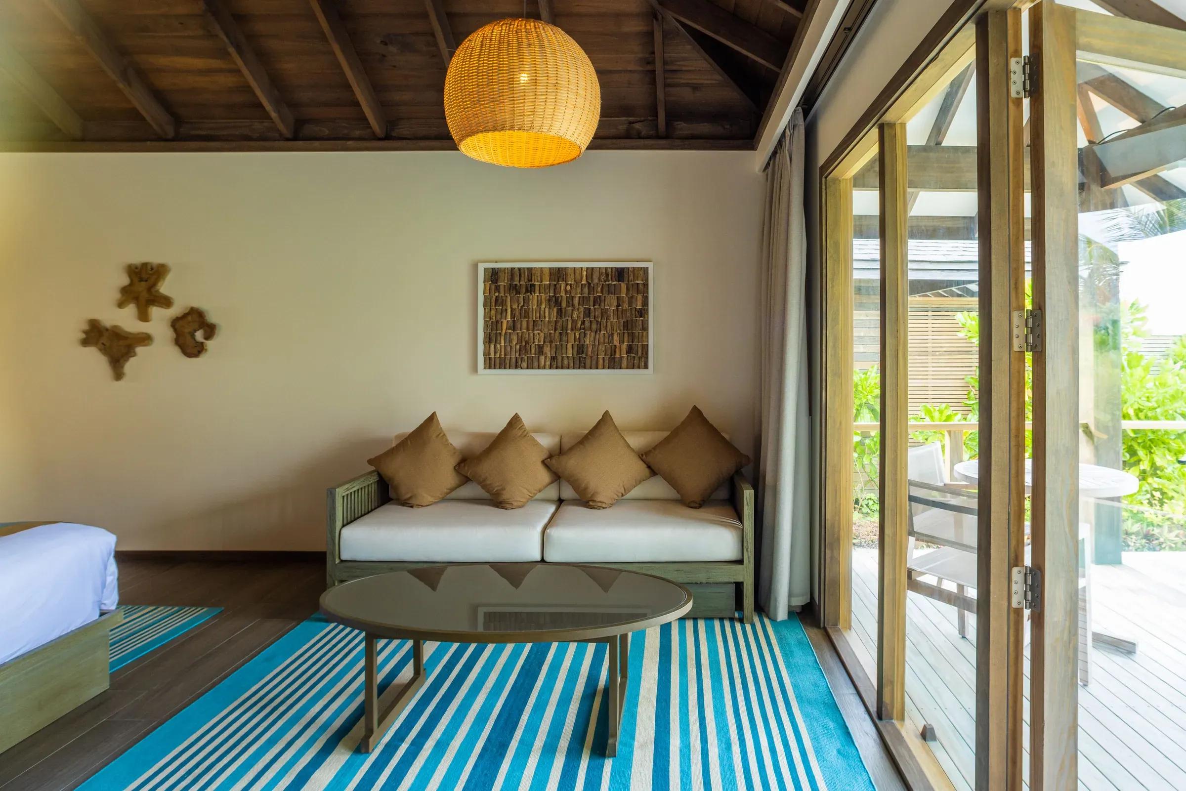 Soggiorno della Dheru Beach Pool Villa con divano e tappeto a righe blu al Jawakara Islands Maldives