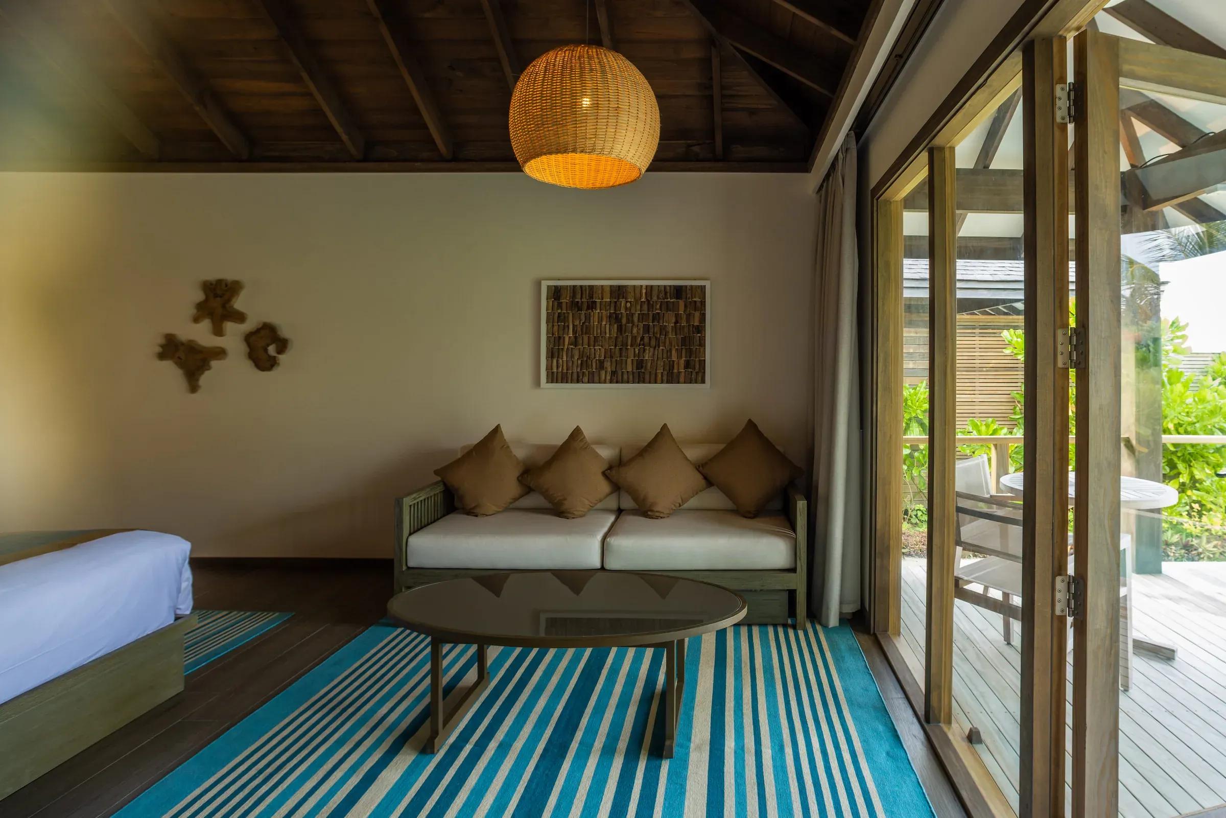 Soggiorno della Dheru Beach Villa con divano, tavolino e accesso alla terrazza al Jawakara Islands Maldives.