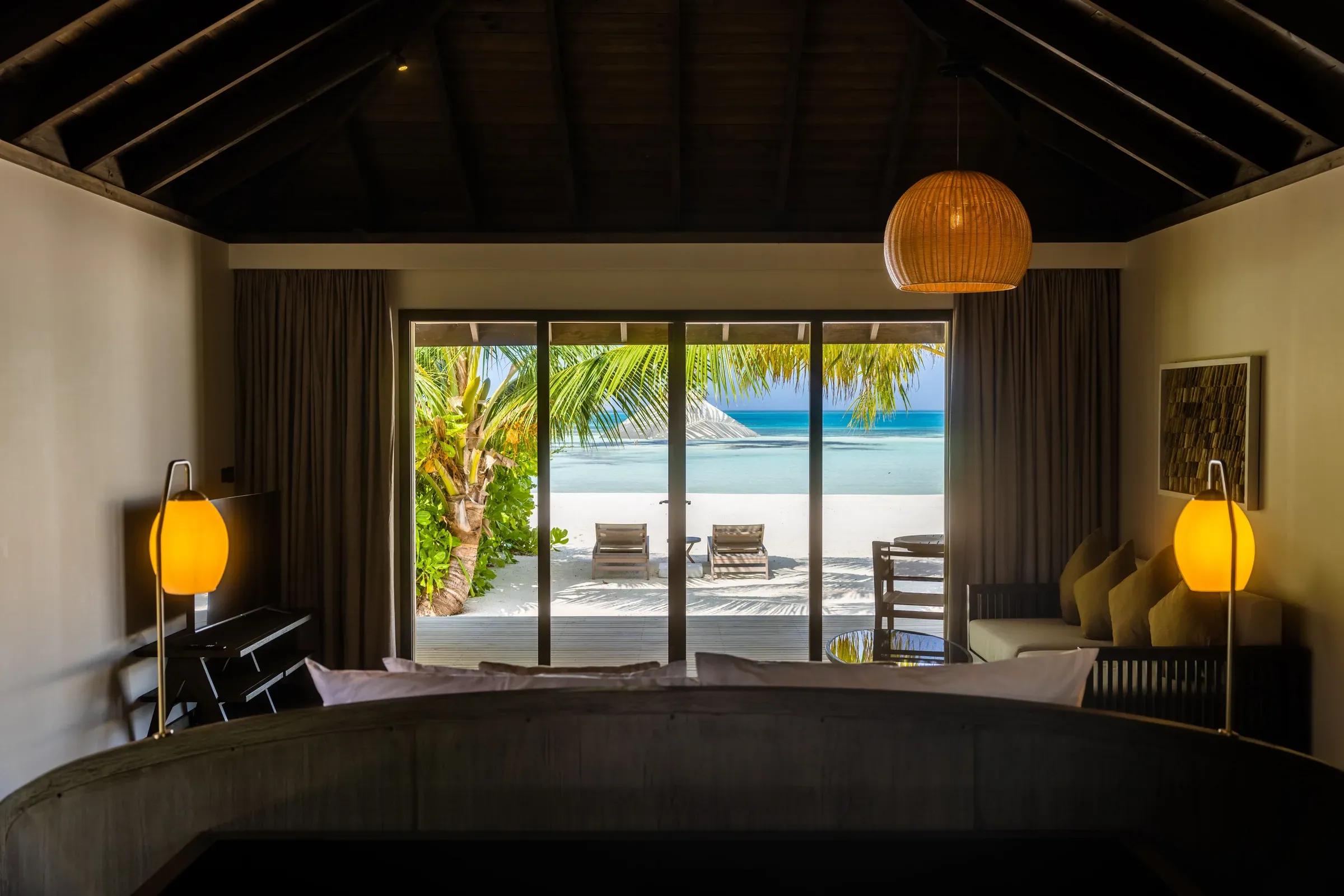 Interno della Dheru Three Bedroom Villa con vista su terrazza, lettini e spiaggia al Jawakara Islands Maldives.