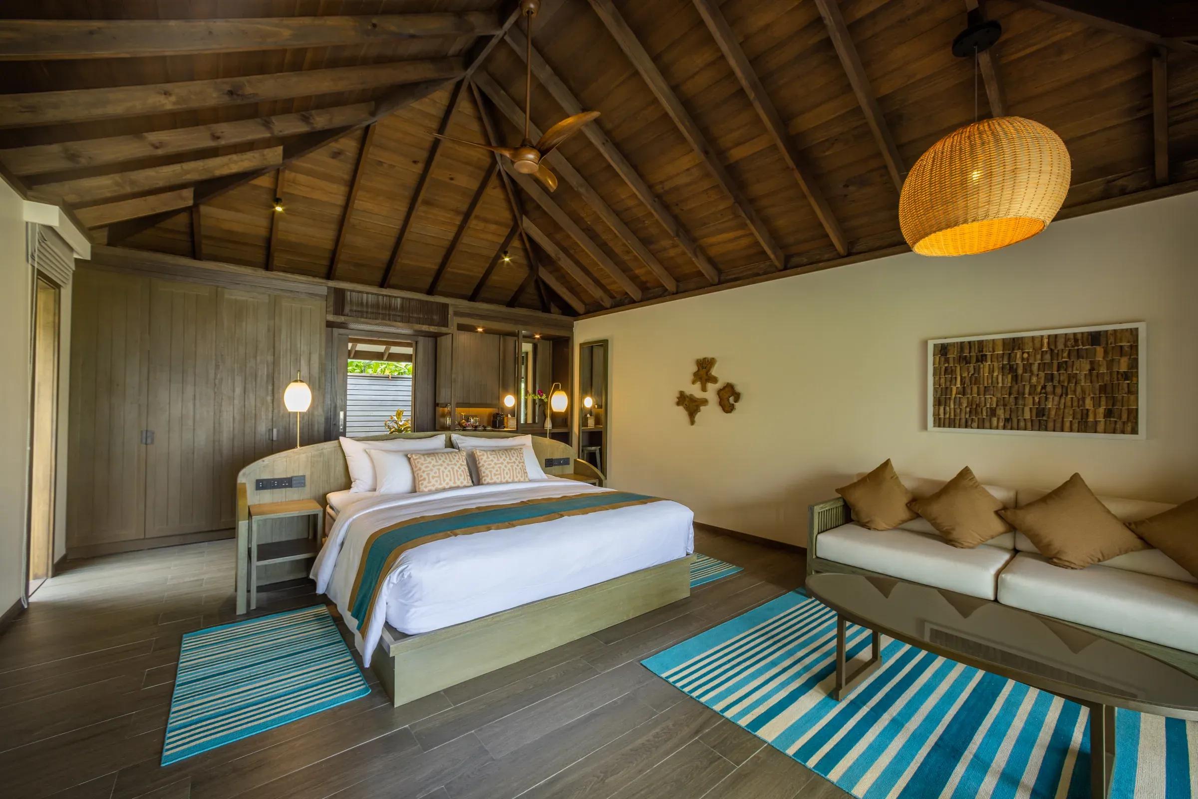 Interno della Mabin Beach Villa con letto matrimoniale e soffitto in legno al Jawakara Islands Maldives.