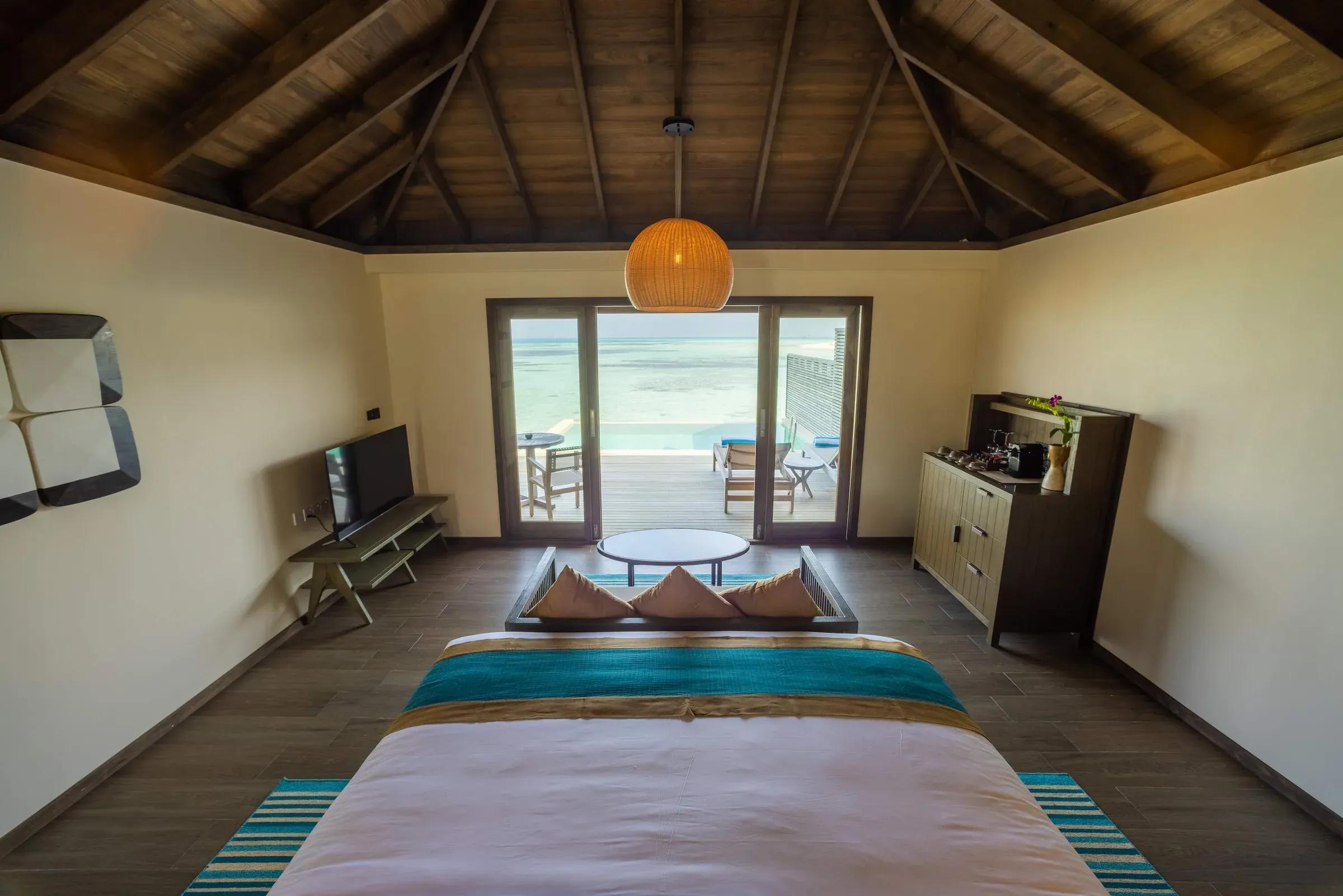 Interno della Mabin Water Pool Villa con letto matrimoniale, TV e vista sulla terrazza e mare al Jawakara Islands Maldives.