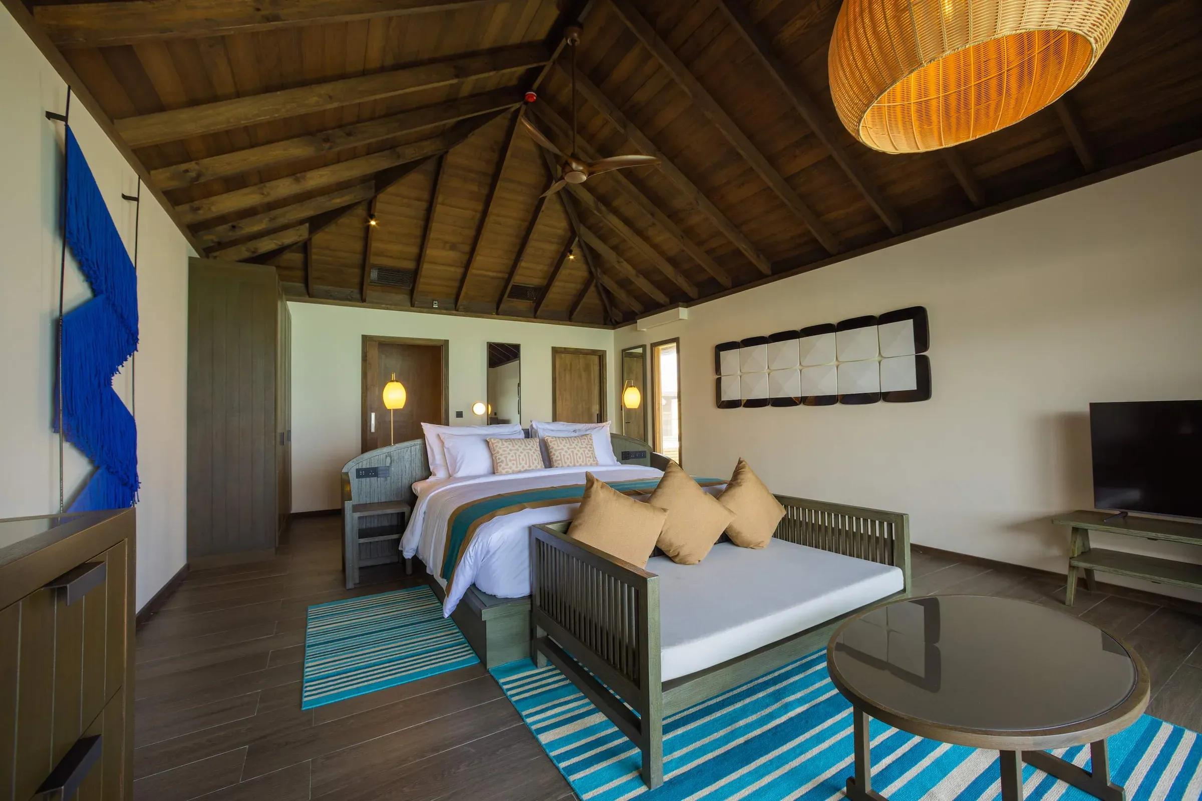Interno della Mabin Water Pool Villa con letto matrimoniale, decorazioni in legno e illuminazione soffusa al Jawakara Islands Maldives.