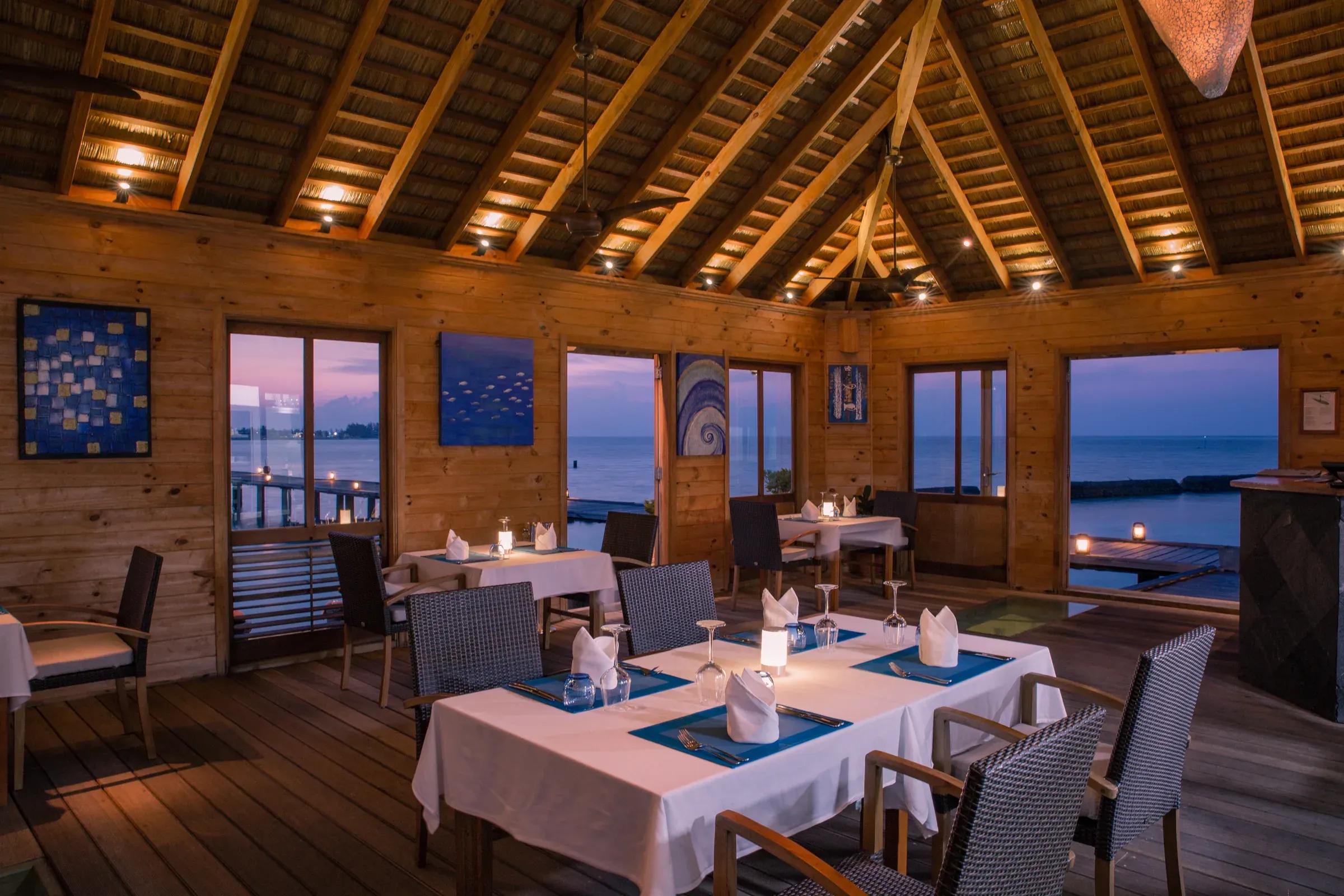 Aqua restaurant con tavoli apparecchiati e vista mare al tramonto al Komandoo Island Resort & Spa