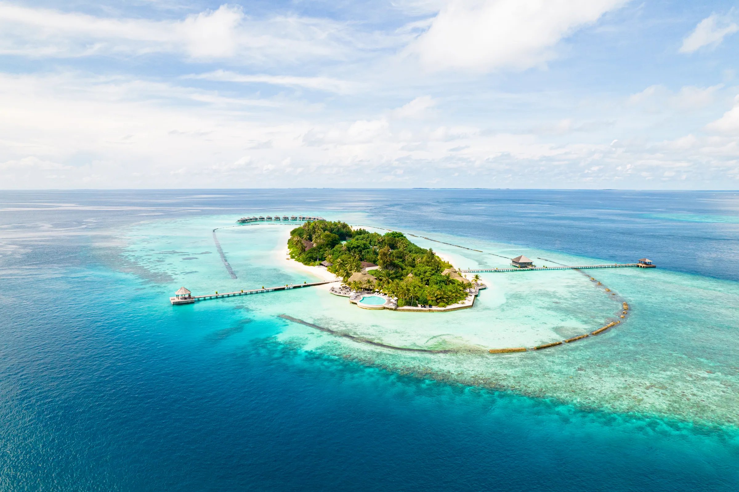 Vista aerea dell'isola tropicale del Komandoo Island Resort & Spa circondata da acque turchesi e barriera corallina.