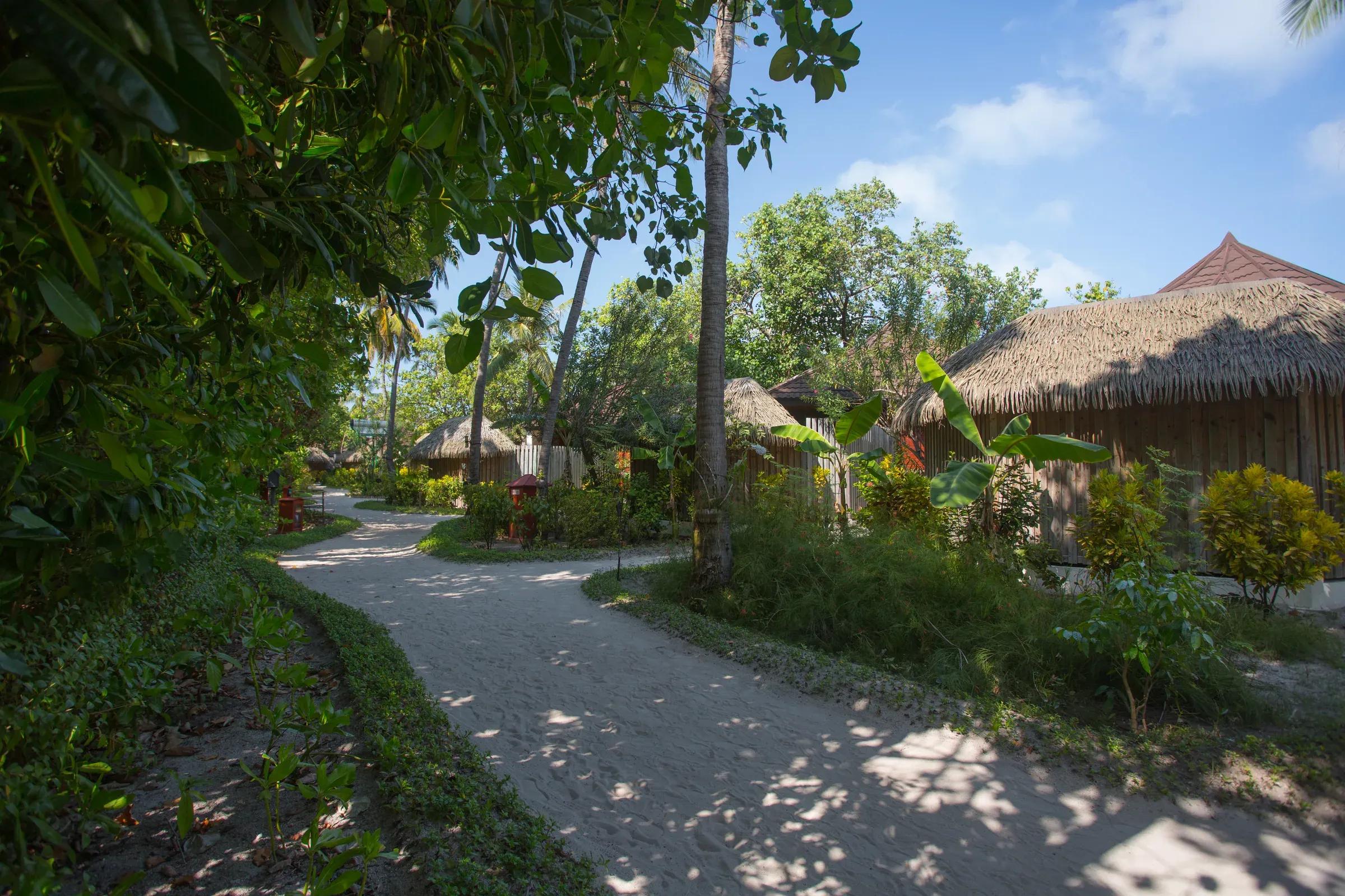 Esterno della Beach Villa con giardino verde e sentiero sabbioso al Komandoo Island Resort & Spa.