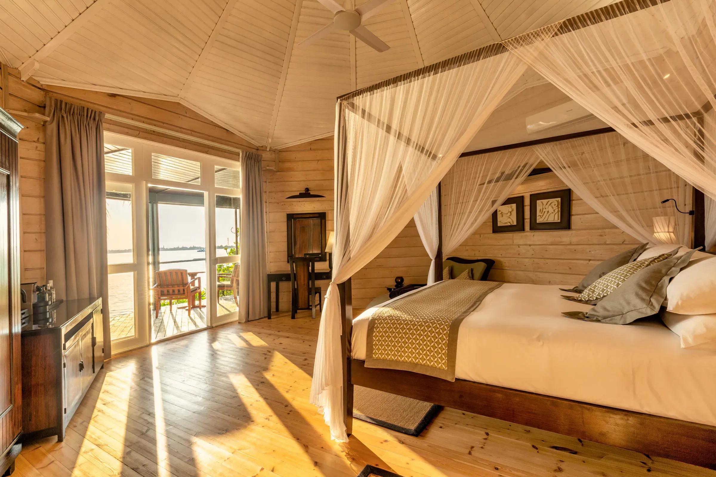 Camera da letto della Jacuzzi Beach Villa con letto a baldacchino e vista sulla terrazza al Komandoo Island Resort & Spa.