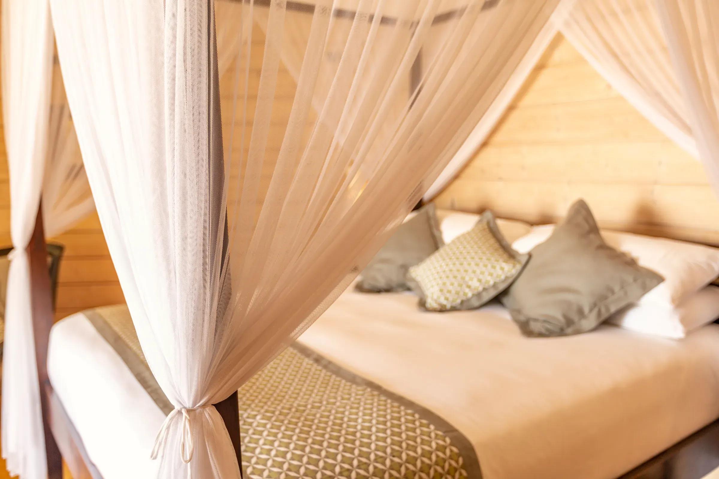 Letto a baldacchino con tende bianche e cuscini decorativi nella Jacuzzi Beach Villa del Komandoo Island Resort & Spa.
