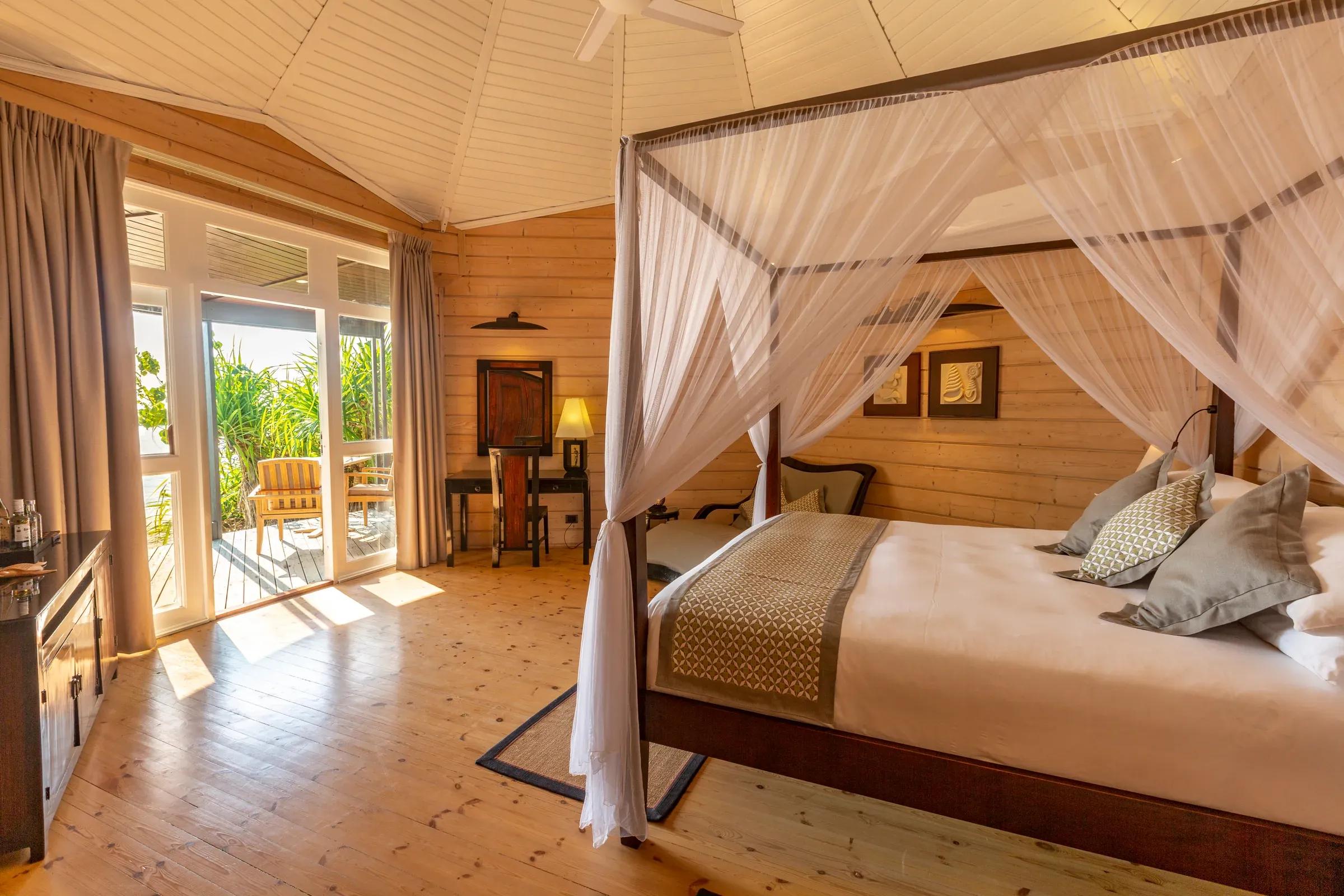 Interno della Jacuzzi Beach Villa con letto a baldacchino e terrazza con sedie al Komandoo Island Resort & Spa.
