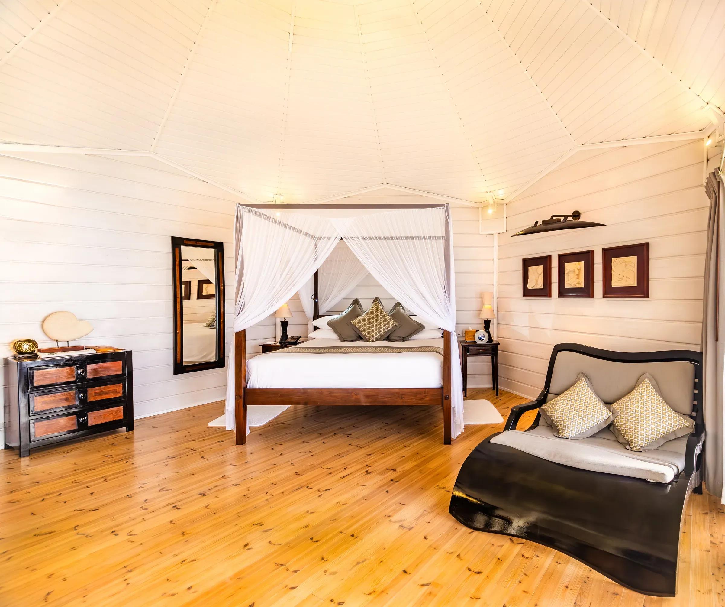 Interno della Jacuzzi Water Villa con letto a baldacchino e poltrona al Komandoo Island Resort & Spa.