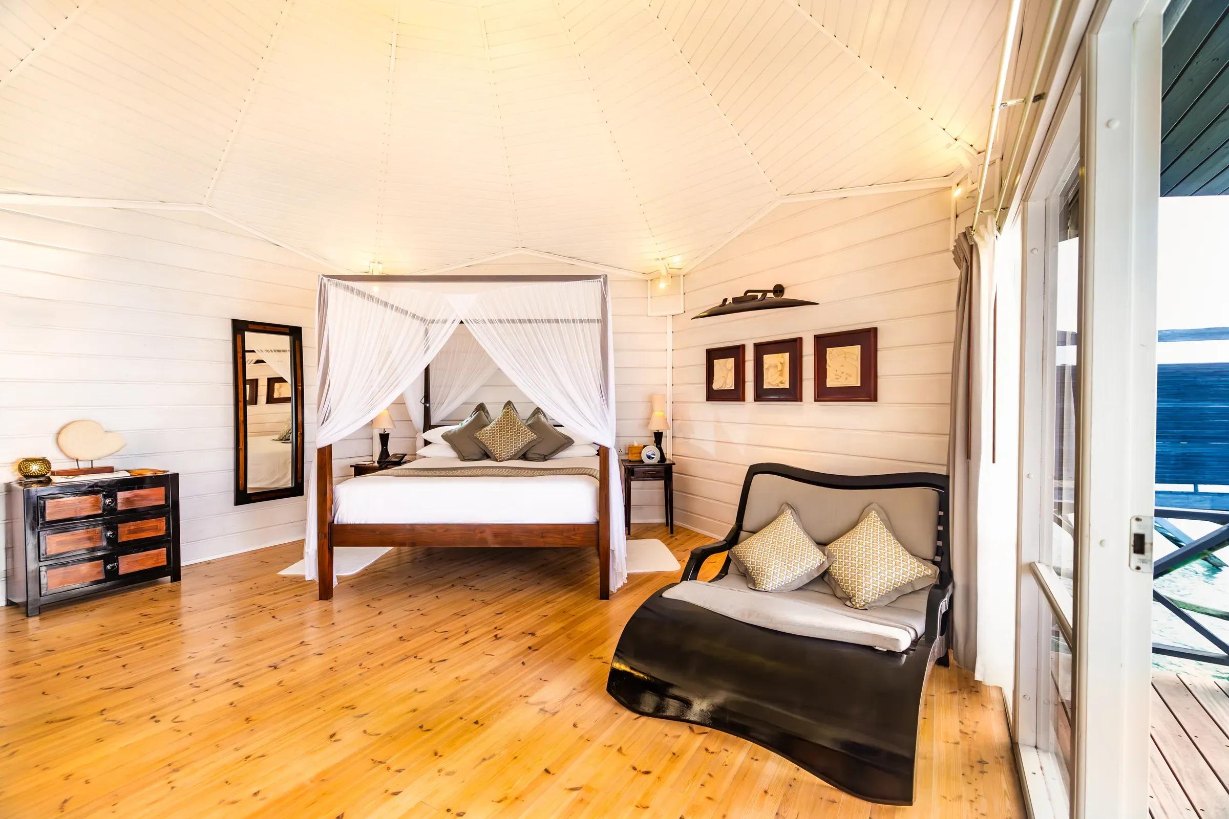 Interno della Ocean Jacuzzi Water Villa con letto a baldacchino e divano al Komandoo Island Resort & Spa.