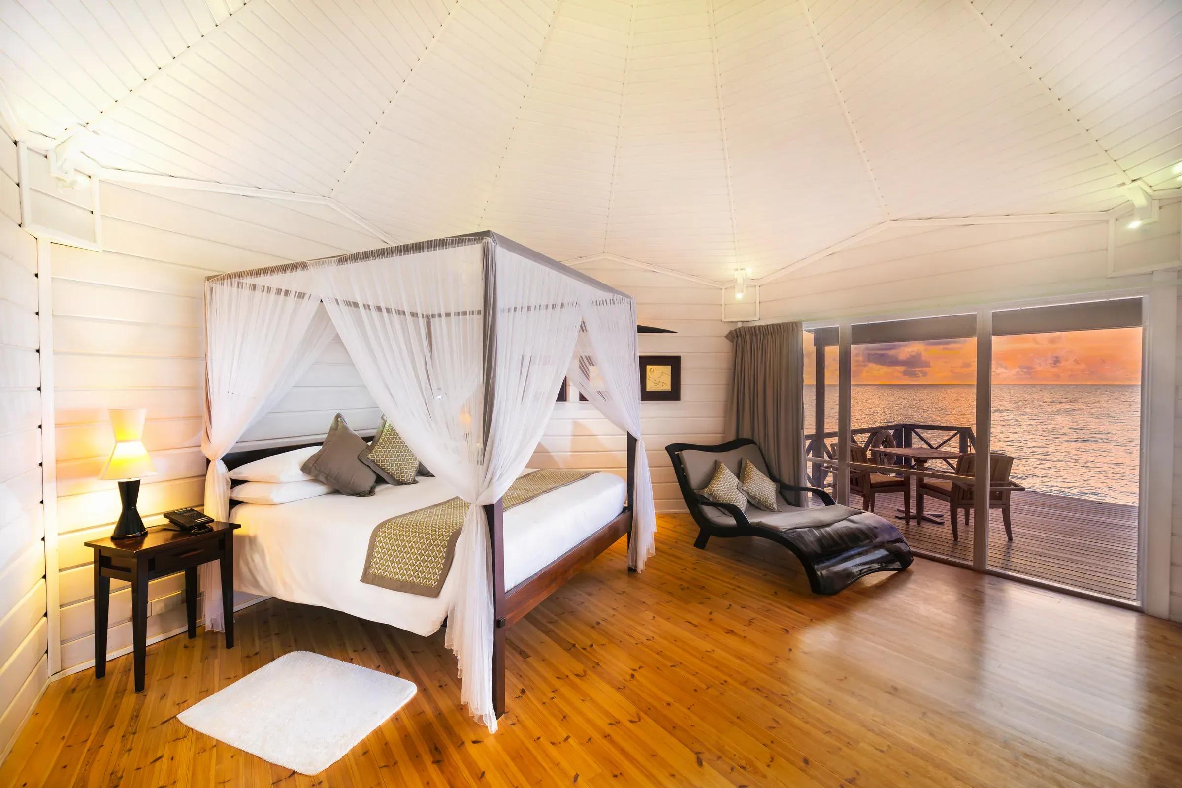 Camera Ocean Jacuzzi Water Villa con letto a baldacchino e vista mare al tramonto presso Komandoo Island Resort & Spa.