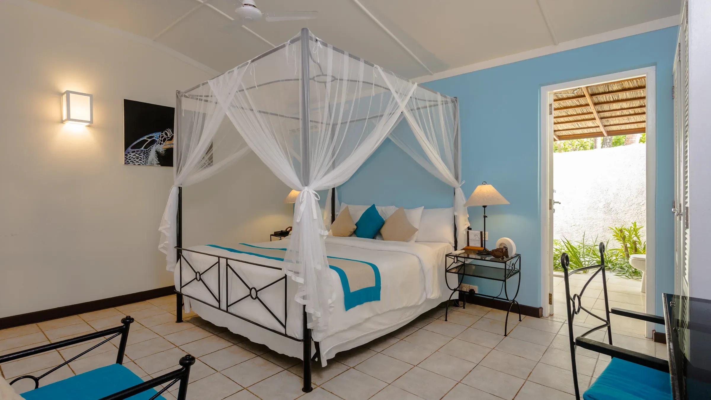 Interno della Beach Bungalow con letto a baldacchino e accesso al patio nel Kuredu Island Resort & Spa.