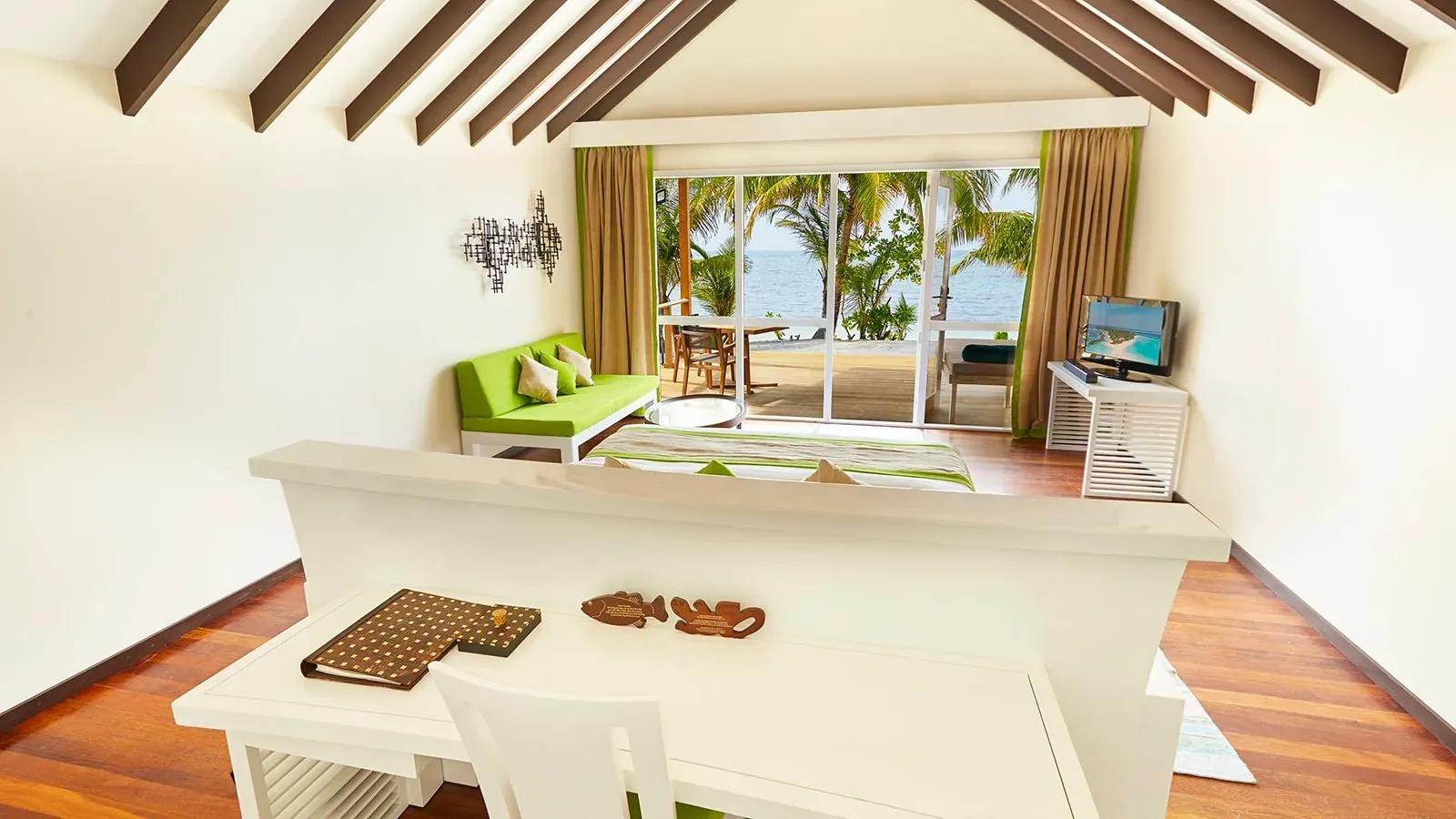 Interno della Deluxe Beach Villa con divano verde e terrazza vista mare al Kuredu Island Resort & Spa.